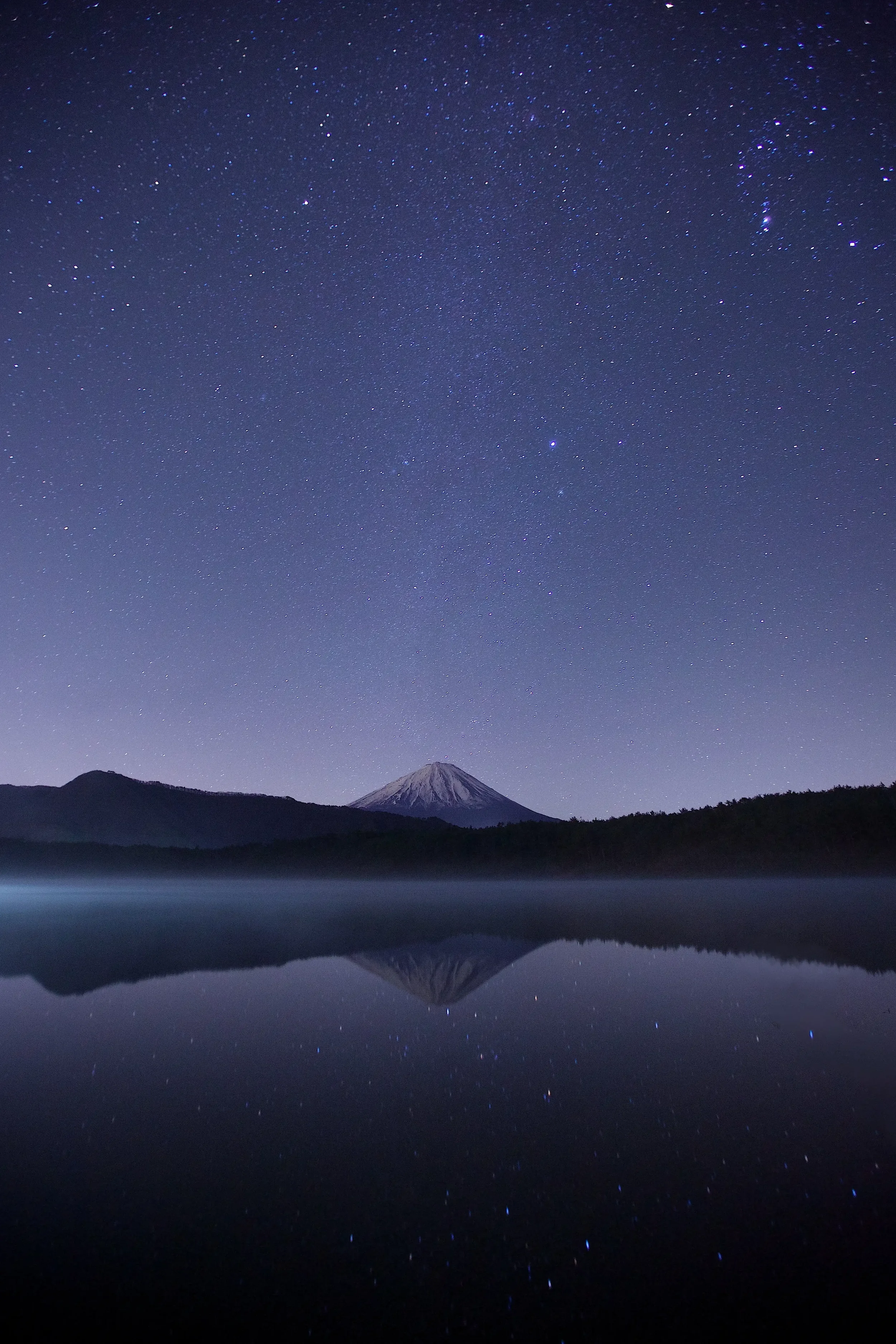 Night sky filled with stars above a mountain reflected in a calm lake.