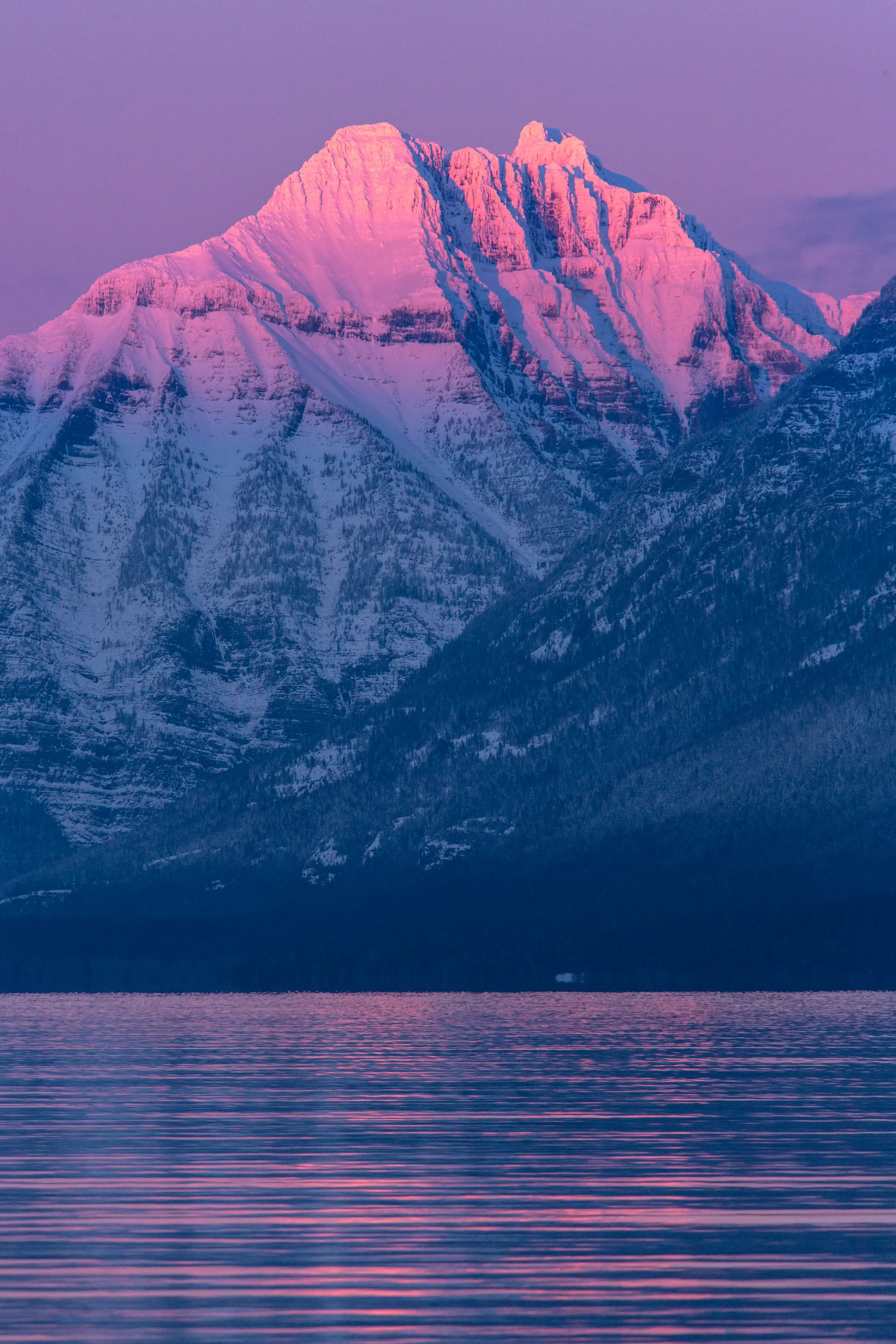 Snow-capped mountain during sunset with pink and purple hues reflected on calm lake water