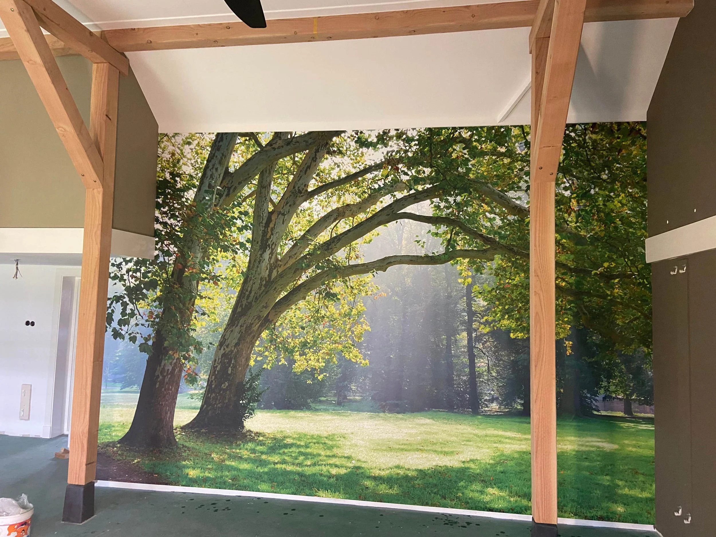 Sunlit forest wall mural wallpaper with lush green trees installed in bright residential space – Pop Papel panoramic nature seamless wallcovering completed project