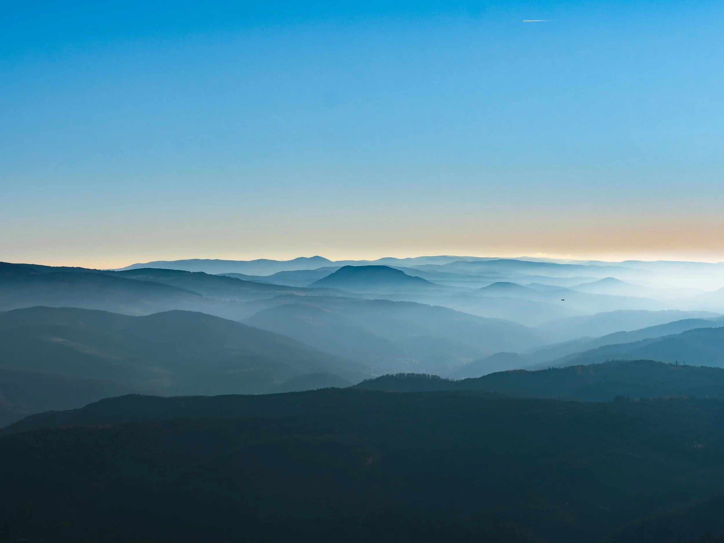 Layered mountain range under a clear sky with a faint contrail.