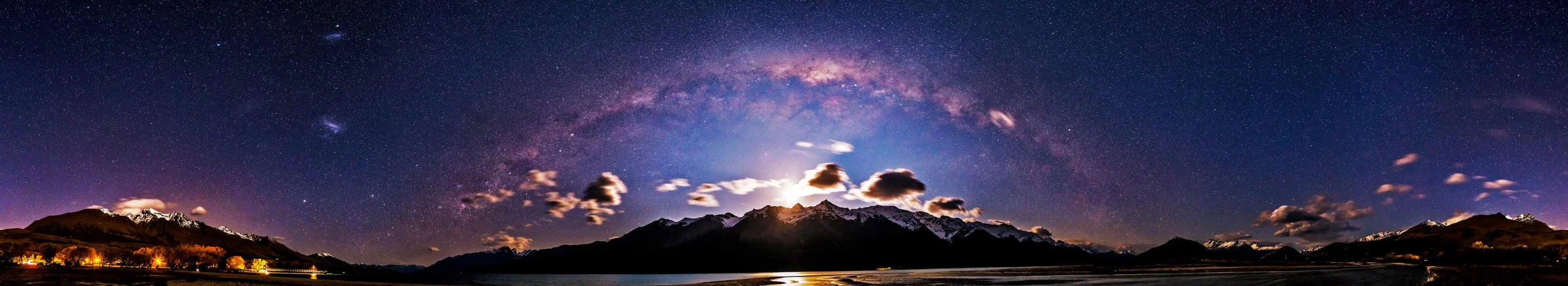 Night sky filled with stars and the Milky Way over mountain range with some clouds illuminated by moonlight.
