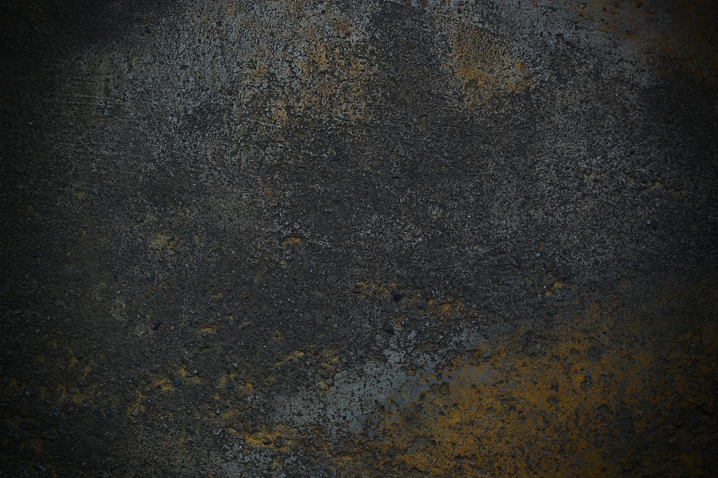 Close-up of a textured, dark, rough surface with patches of orange and gray, resembling a weathered or corroded metal or stone material.