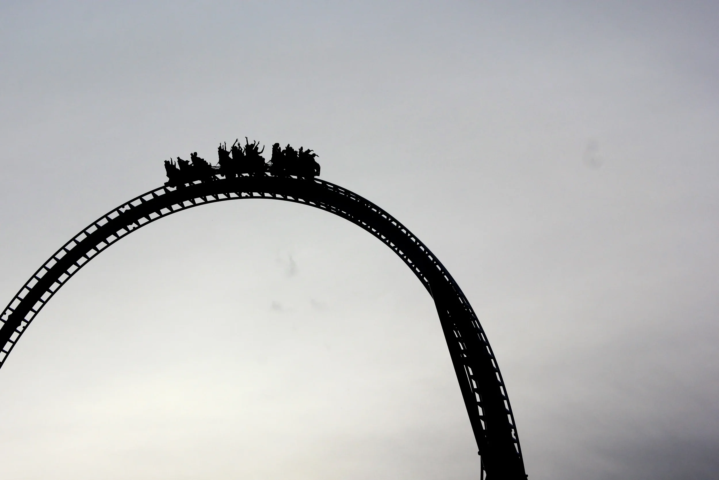 Silhouette of people on a roller coaster against a cloudy sky.