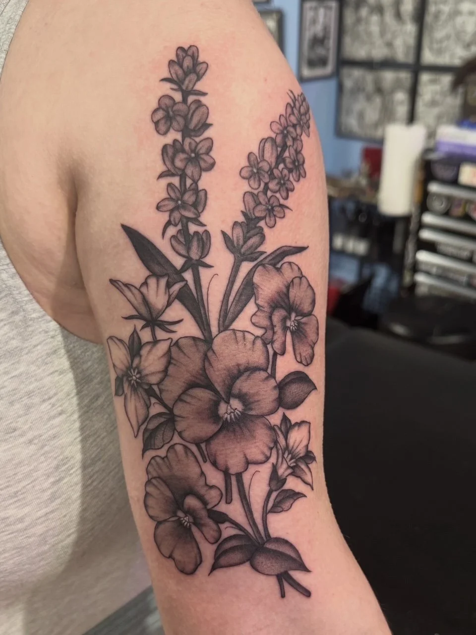 Black and gray floral tattoo with pansies, lavender, and other flowers on upper arm.