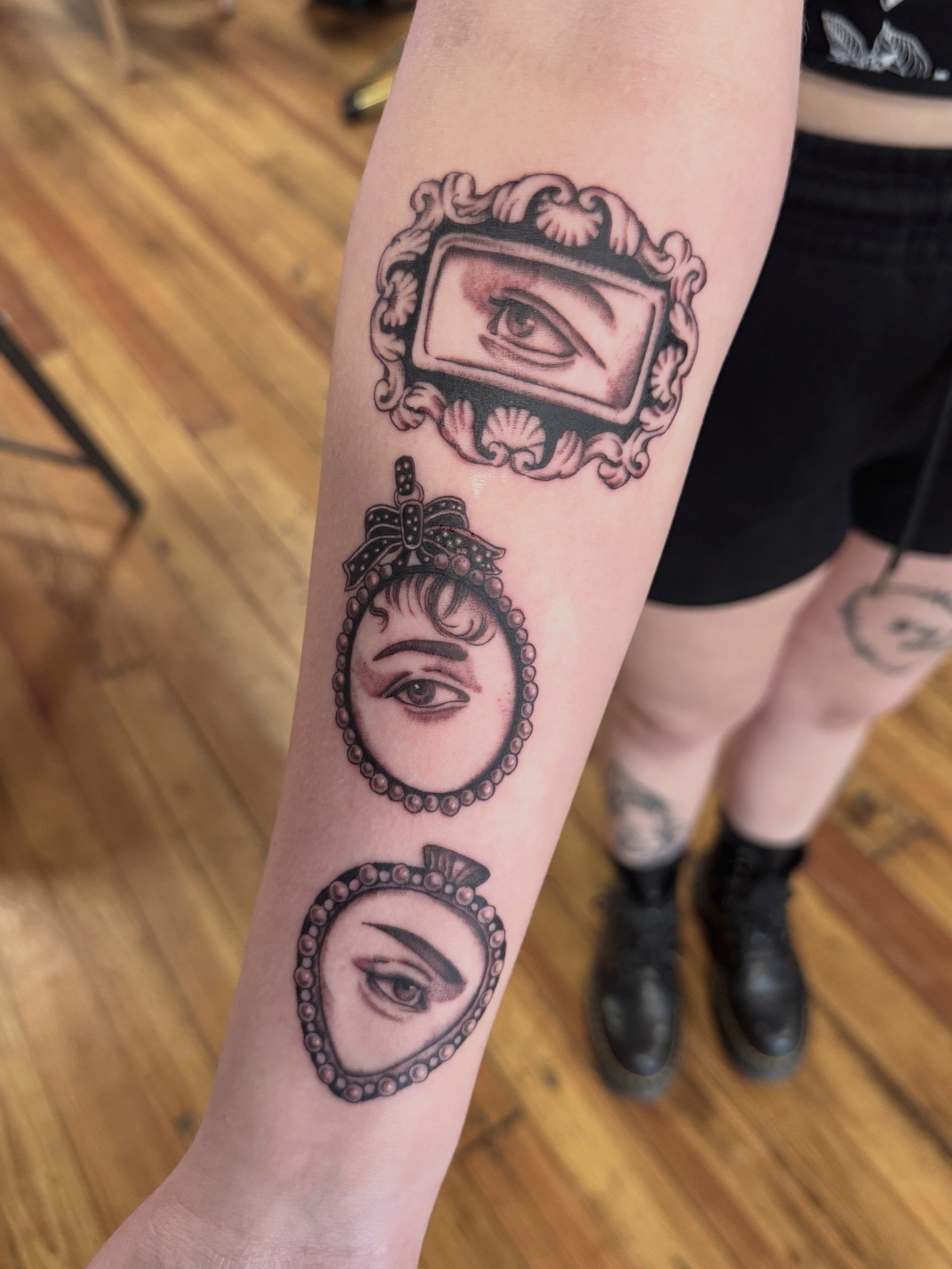 Tattoo of Victorian eyes inside a decorative frame on person's forearm.
