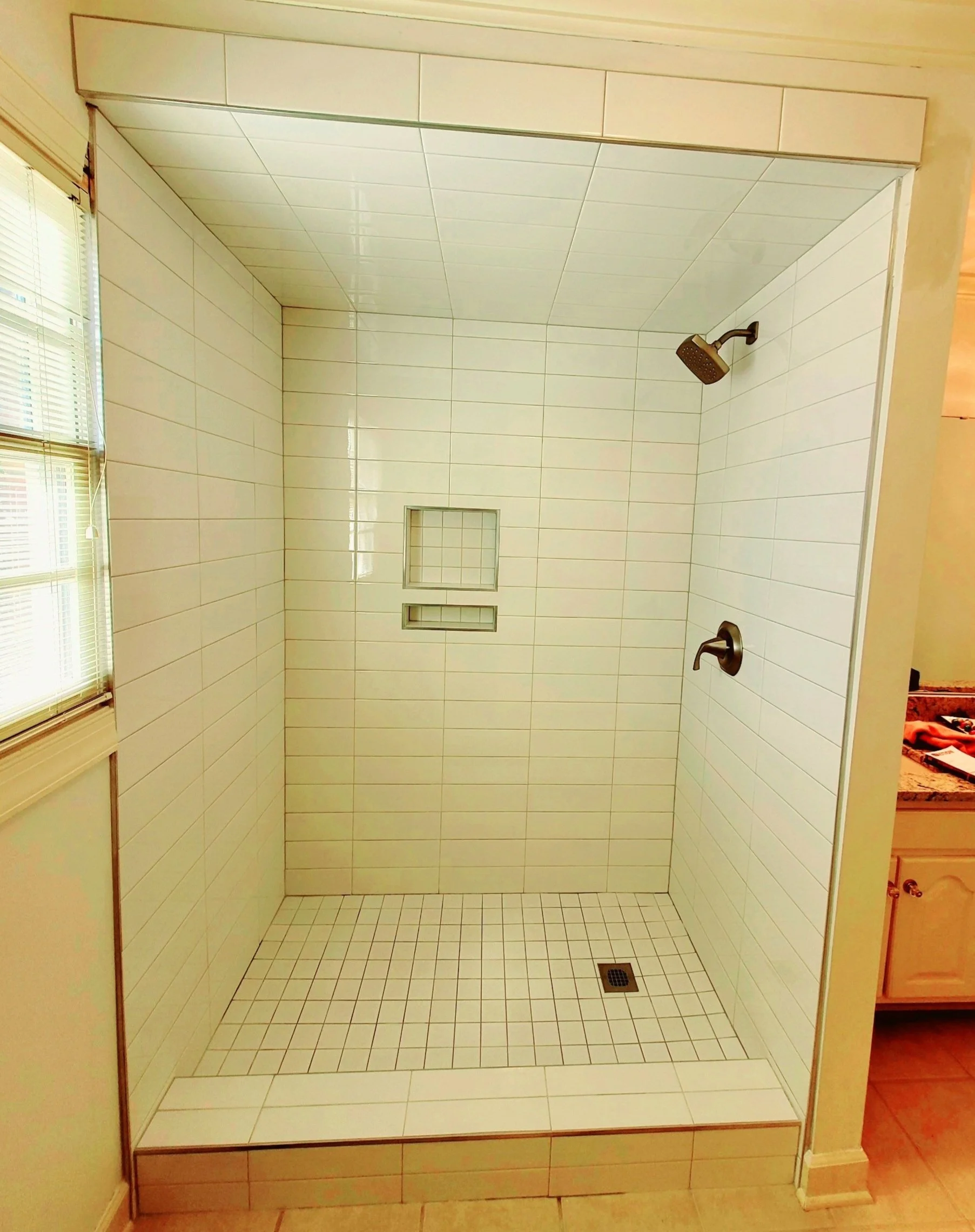 Finished walk-in tile shower with recessed niche, tiled shower floor and shower fixtures
