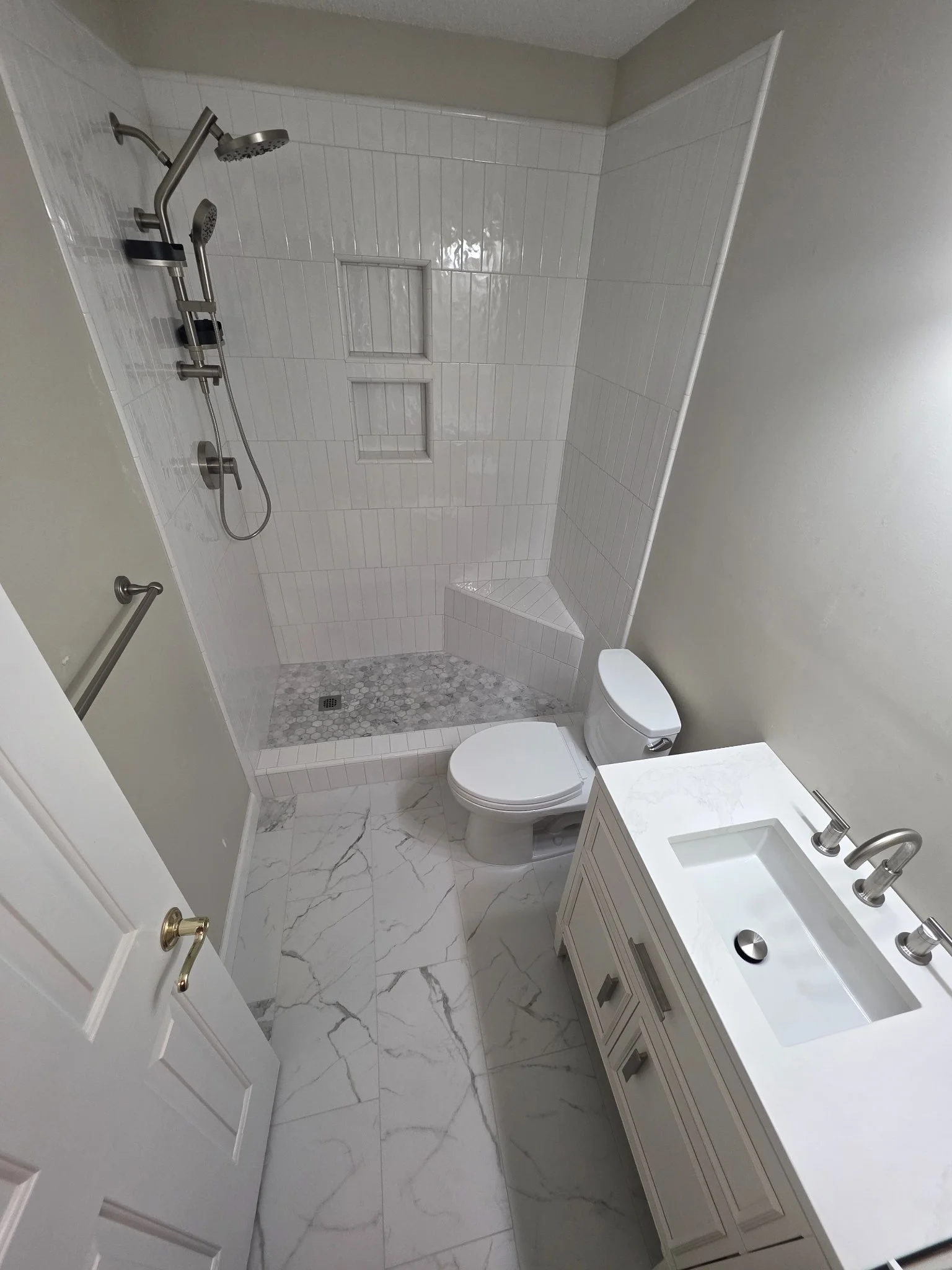 Full bathroom remodel in Greensboro, NC — white subway tile shower with bench and niches, vanity, and marble-look floor by Floors 'N More