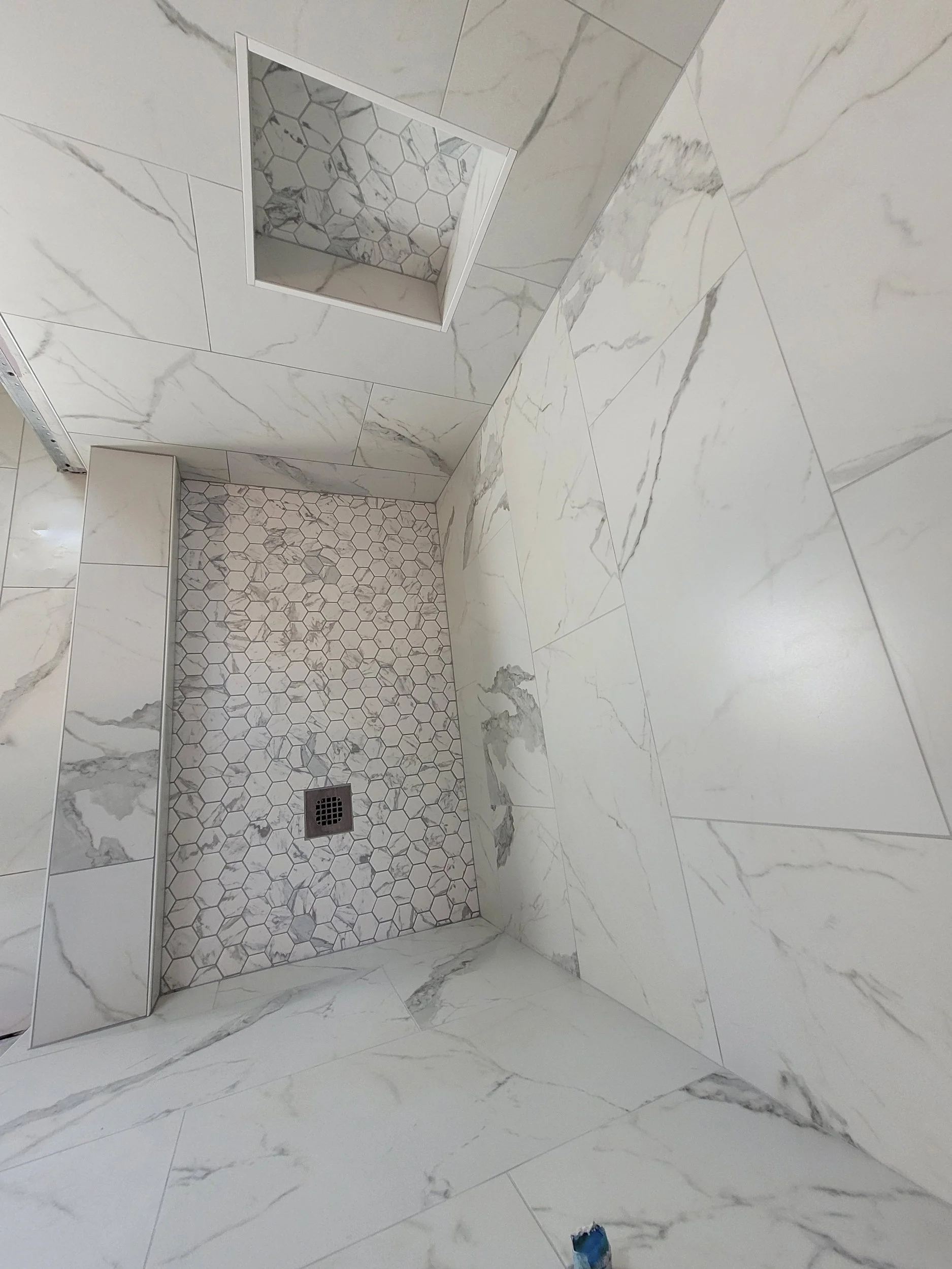Finished custom tile shower with recessed mosaic tile niche and large-format wall tile