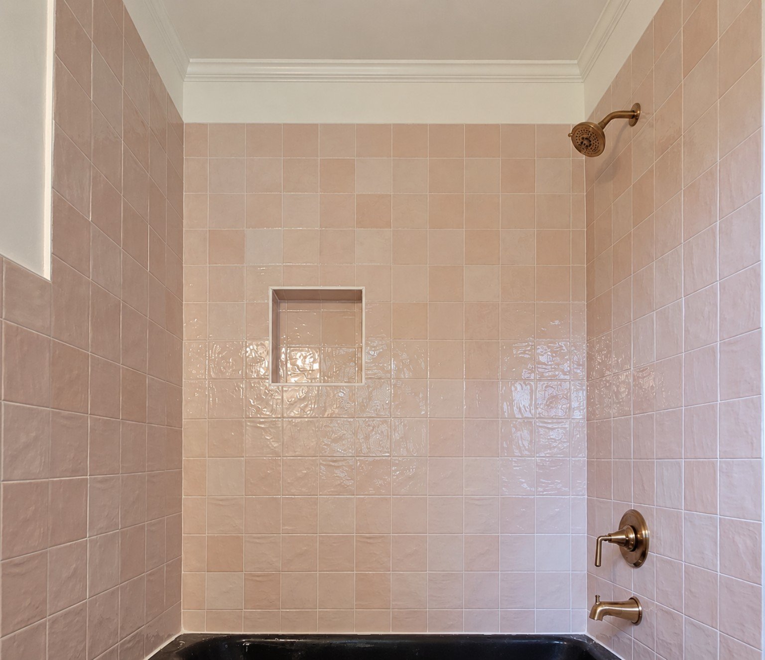 Beige square-tile tub surround with a recessed niche, bronze shower fixtures, and white crown molding