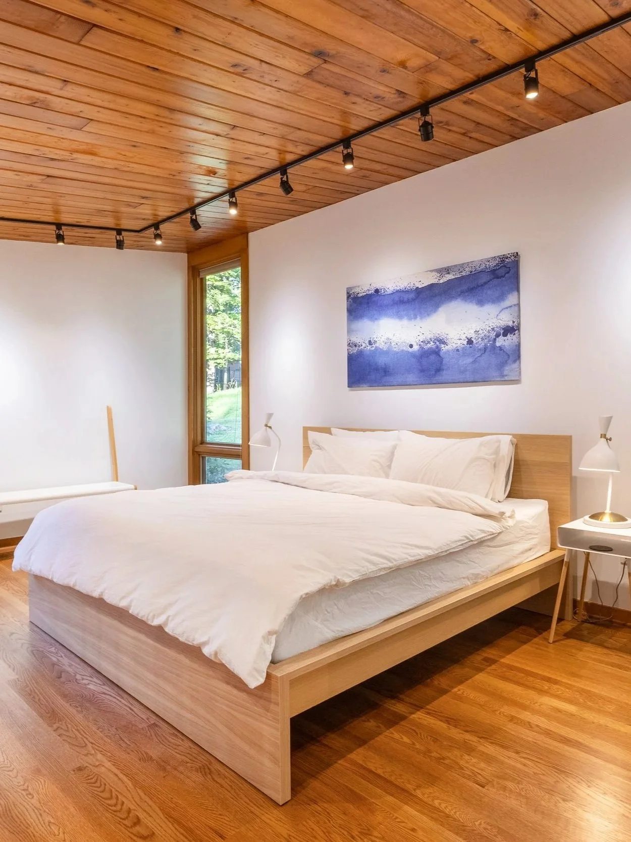 Mid-century modern bedroom film location with wood-paneled ceiling, hardwood floors, large windows with natural light, and serene wooded views.