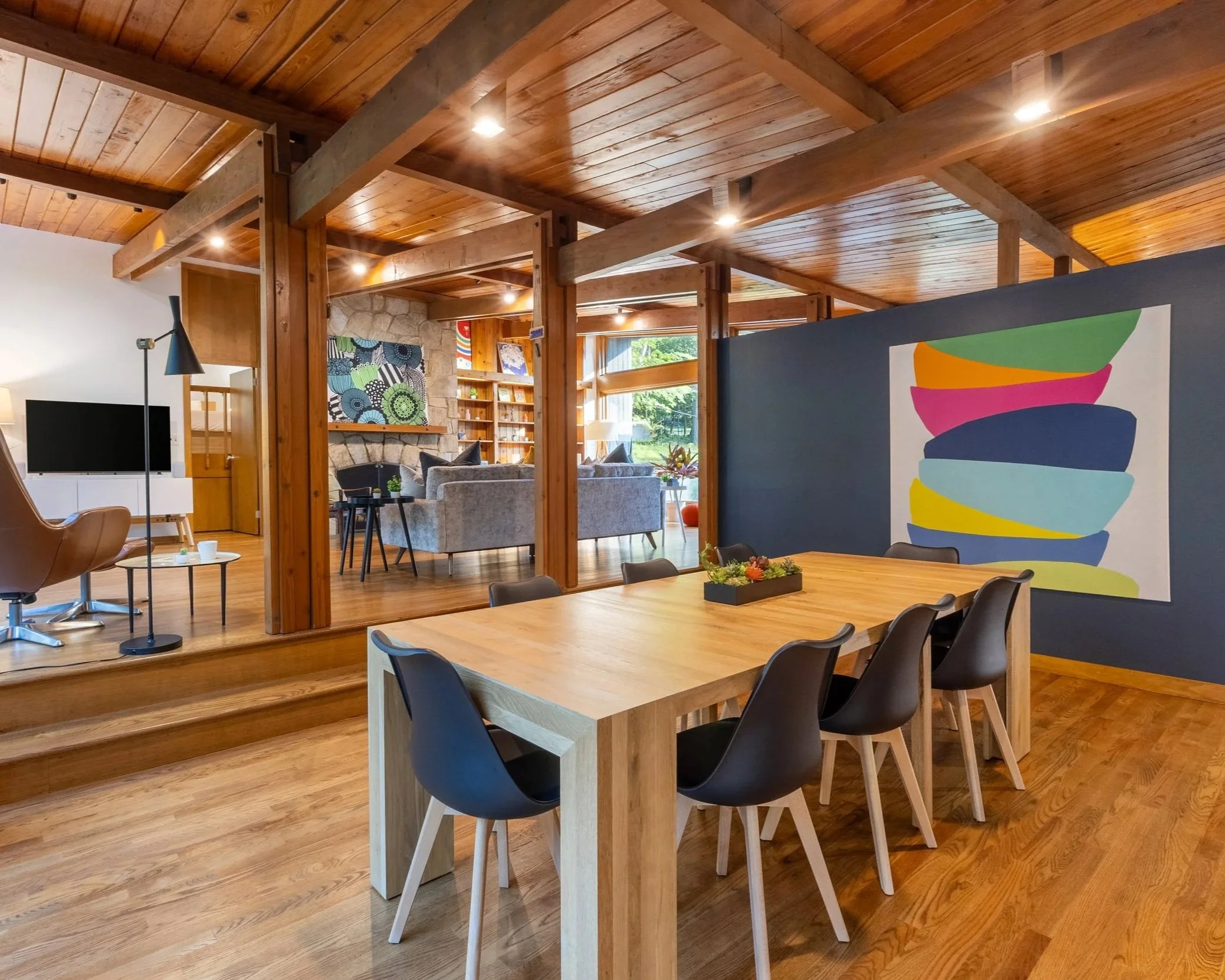 Mid-century modern open-concept living and dining area in New Jersey film location with vaulted redwood ceiling, fieldstone fireplace, and glass wall views.