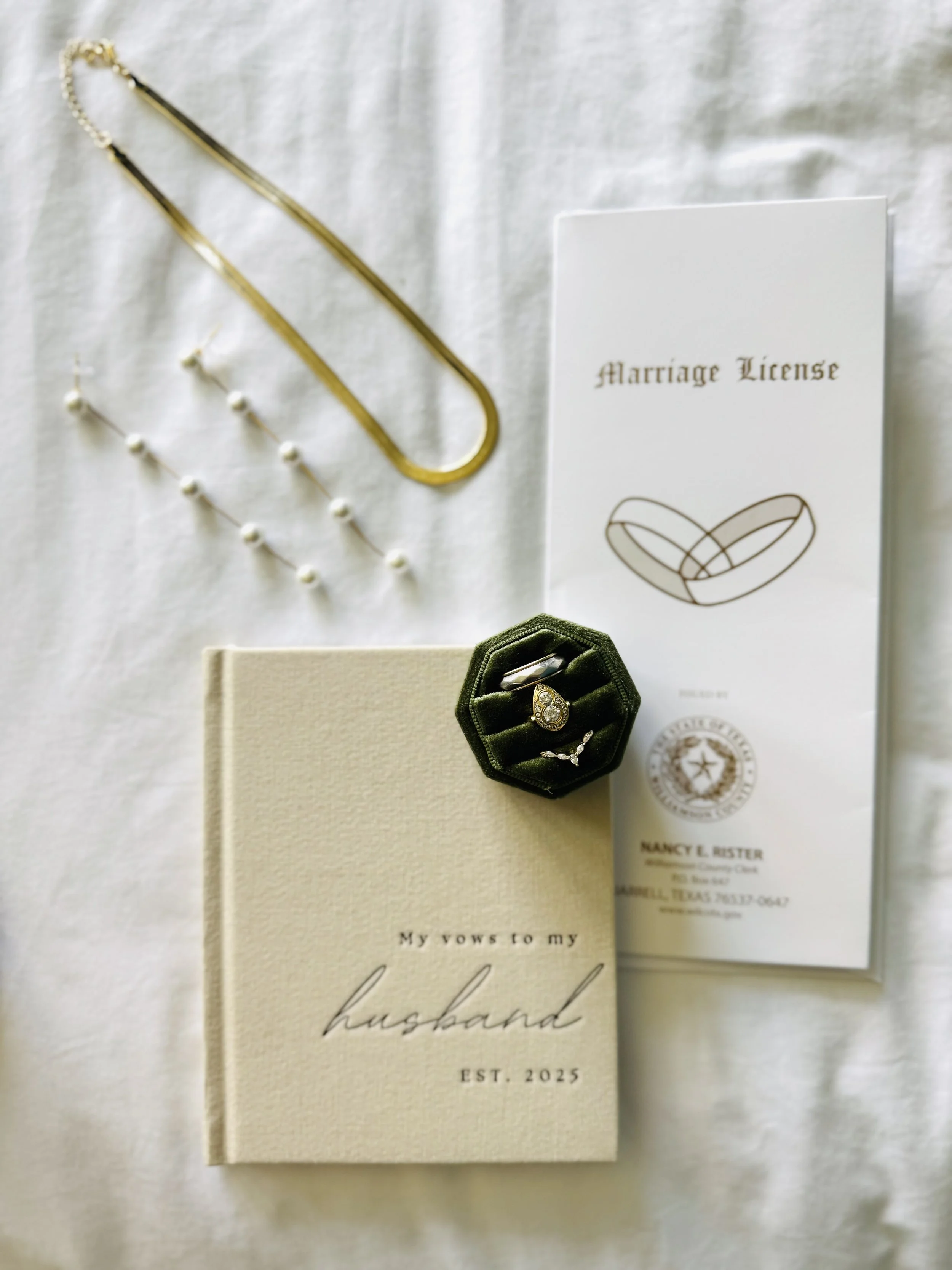 Wedding jewelry and documents, including a pearl necklace, pearl earrings, a wedding ring in a green velvet box, a marriage license, and a vow book