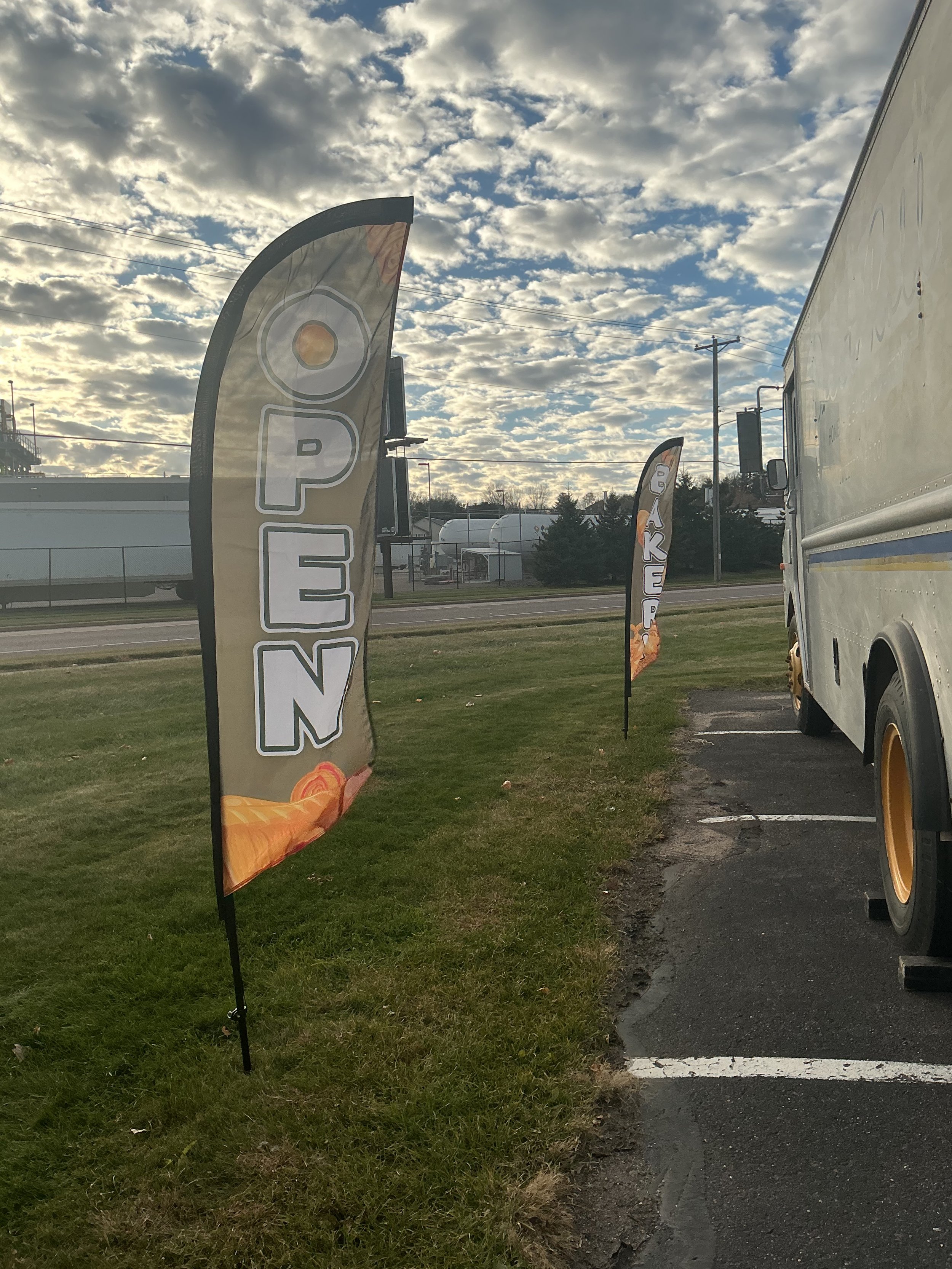 Two flags display the word 'OPEN' next to a food truck, with a partly cloudy sky and some trees in the background.