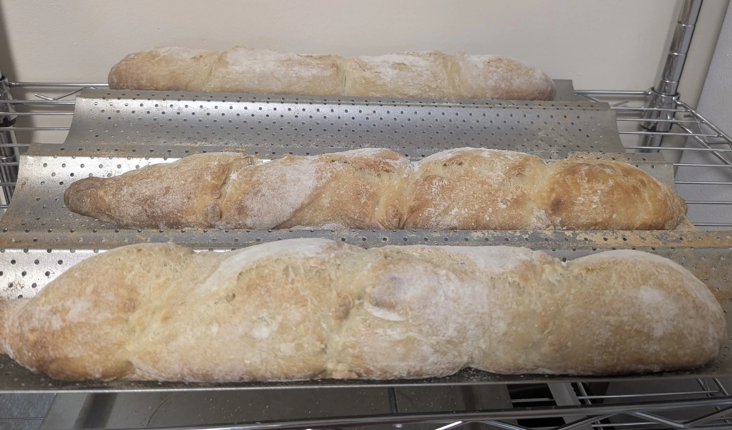 Three loaves of bread resting on metal racks lined with parchment paper.