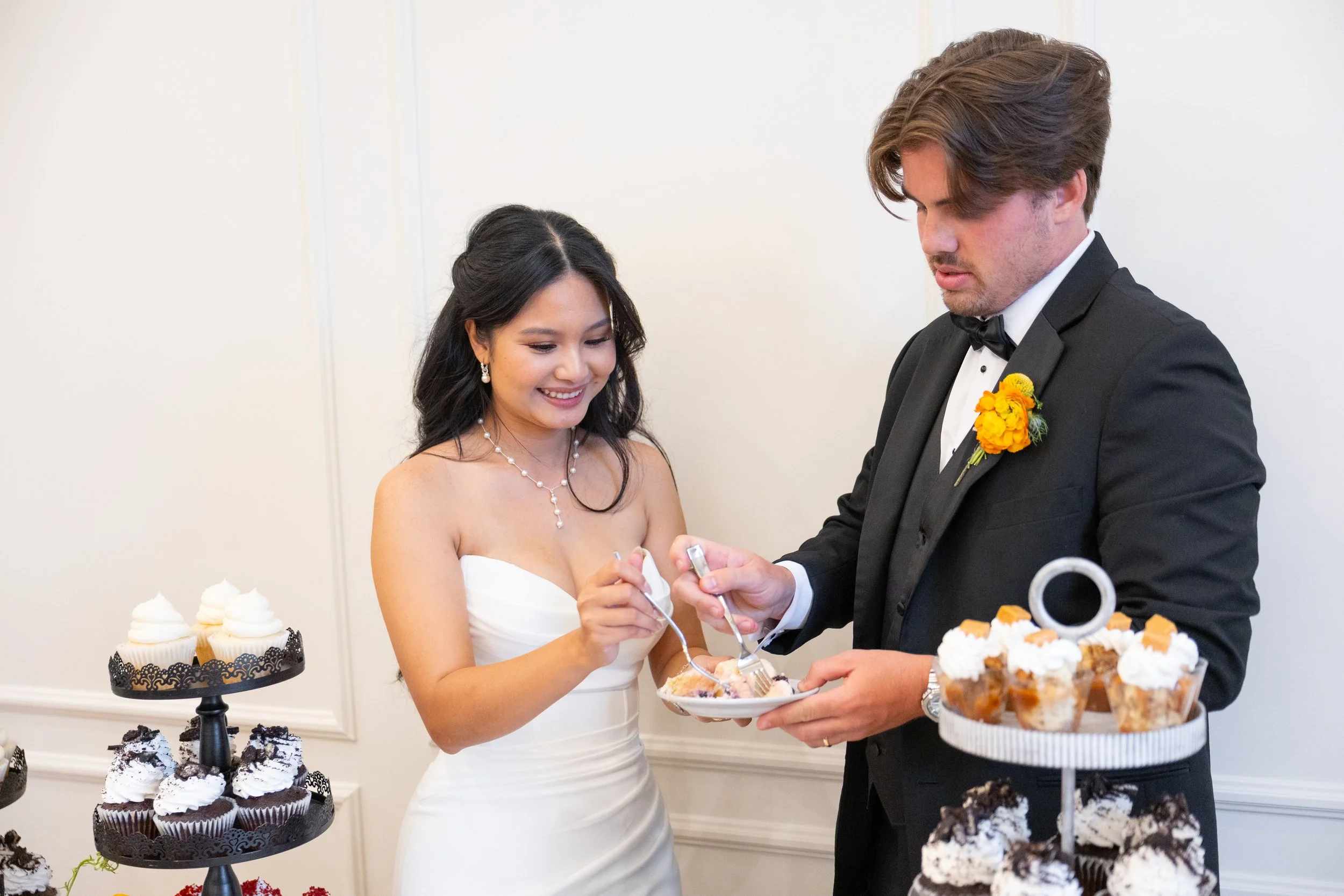 A bride and groom sharing a moment during their wedding cake cutting ceremony, with desserts and cupcakes displayed on tiers around them.
