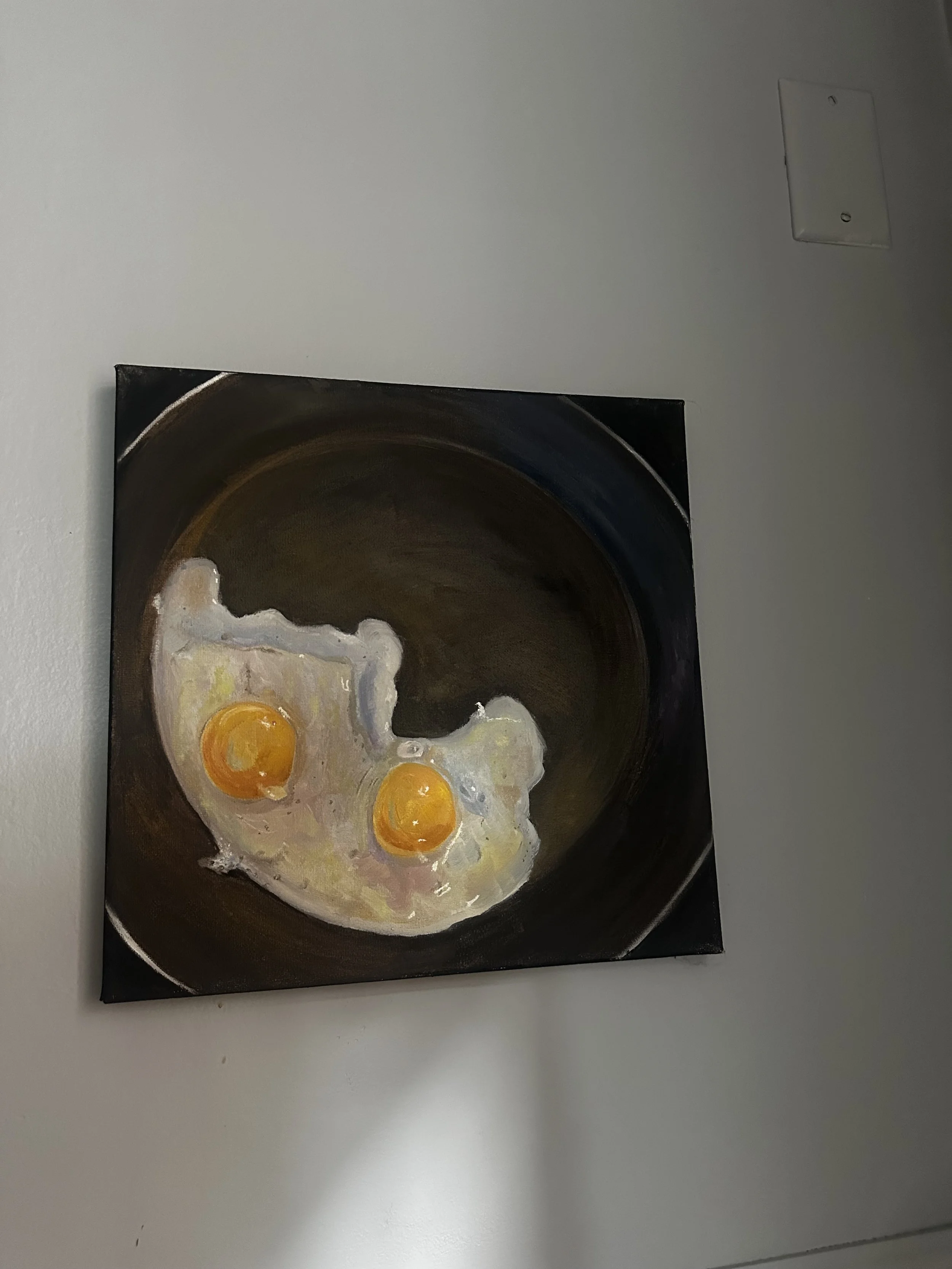 Painting of two sunny-side-up eggs cooking in a frying pan on a gray wall.