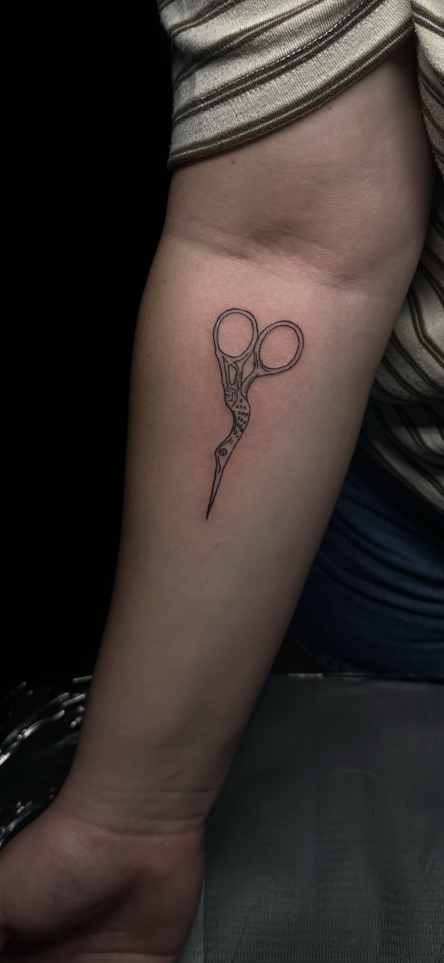 Tattoo of a pair of scissors on a person's forearm.