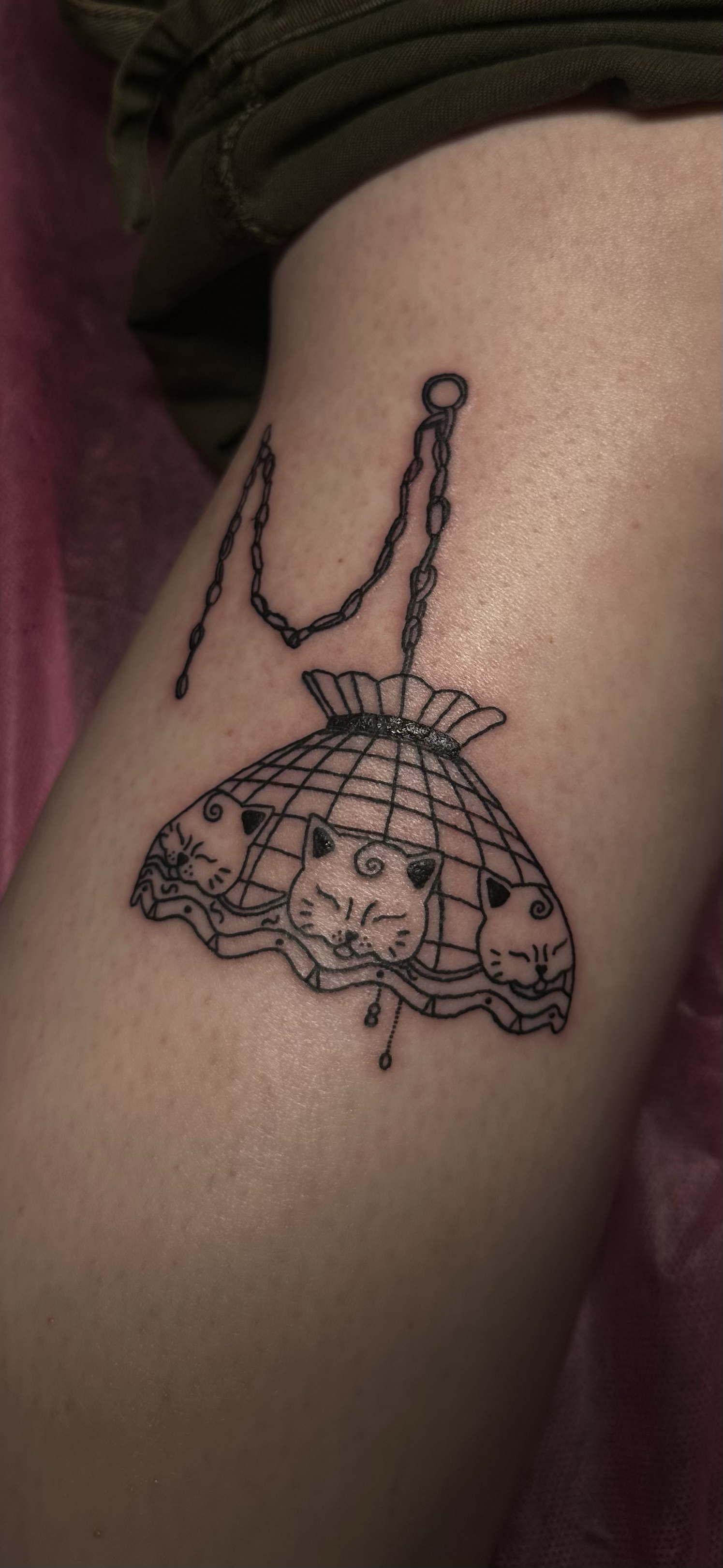 Tattoo of a domed cat cage with three cats inside, surrounded by a chain and a clasp, on person's skin.