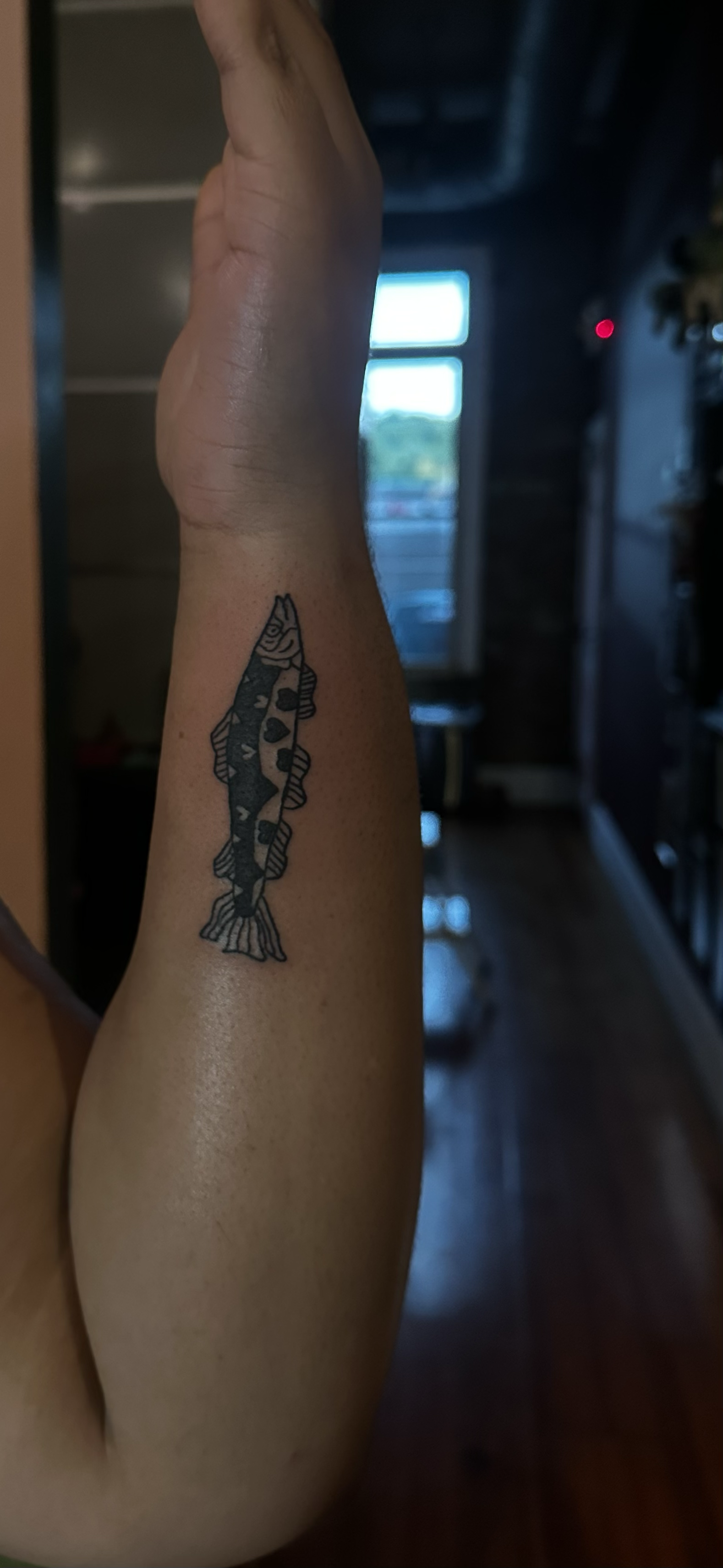 A person's arm with a black and white tattoo of a fish.