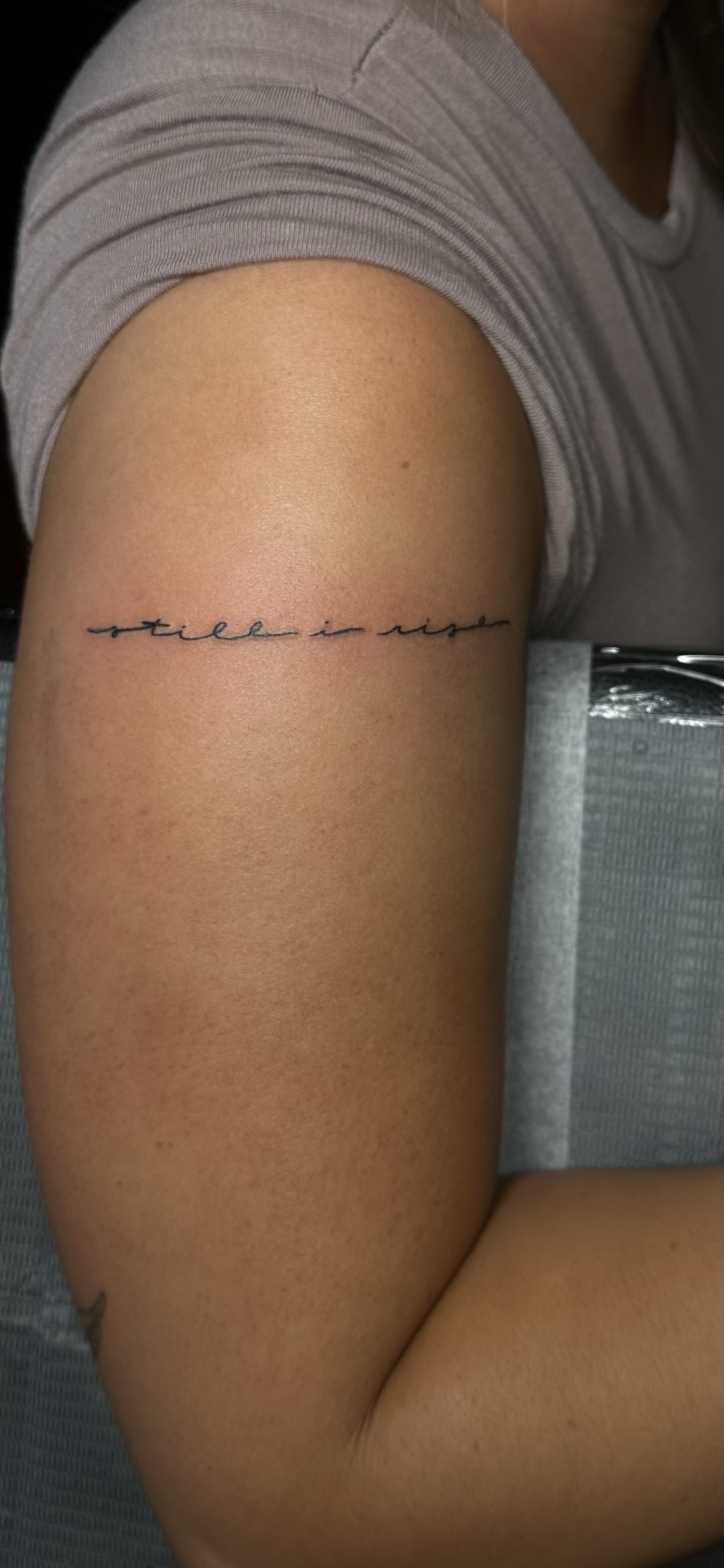 Tattoo on person's arm with the phrase 'still in rise' in cursive script.