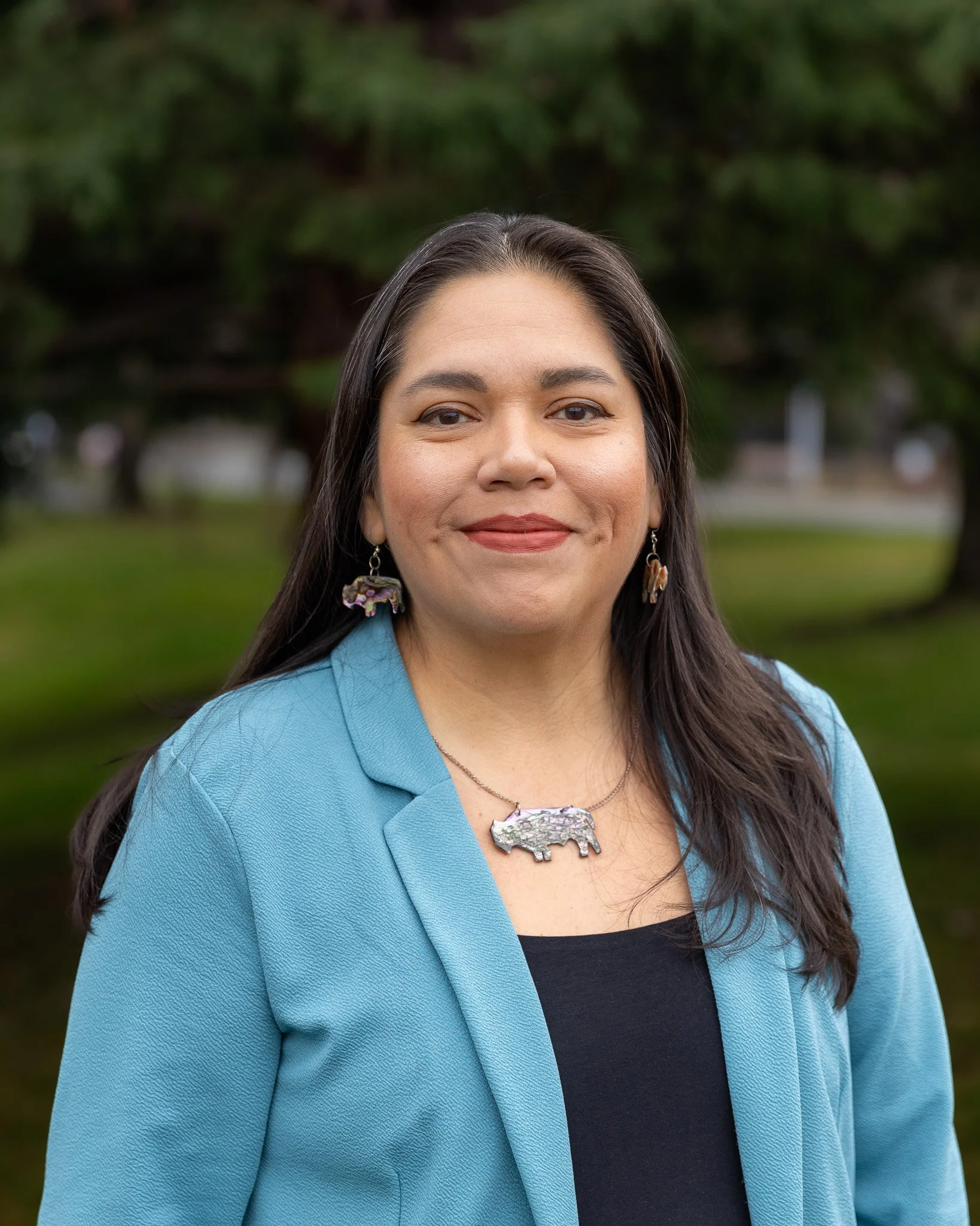 A woman smiling and sitting on a green couch in a room with colorful pillows and a large abstract painting on the wall.