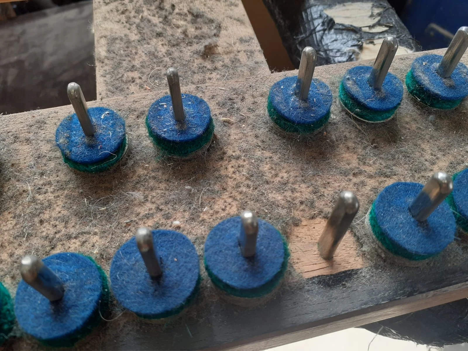 Multiple felt pads with metal pins inserted, arranged on a workbench in a woodworking or craft shop.