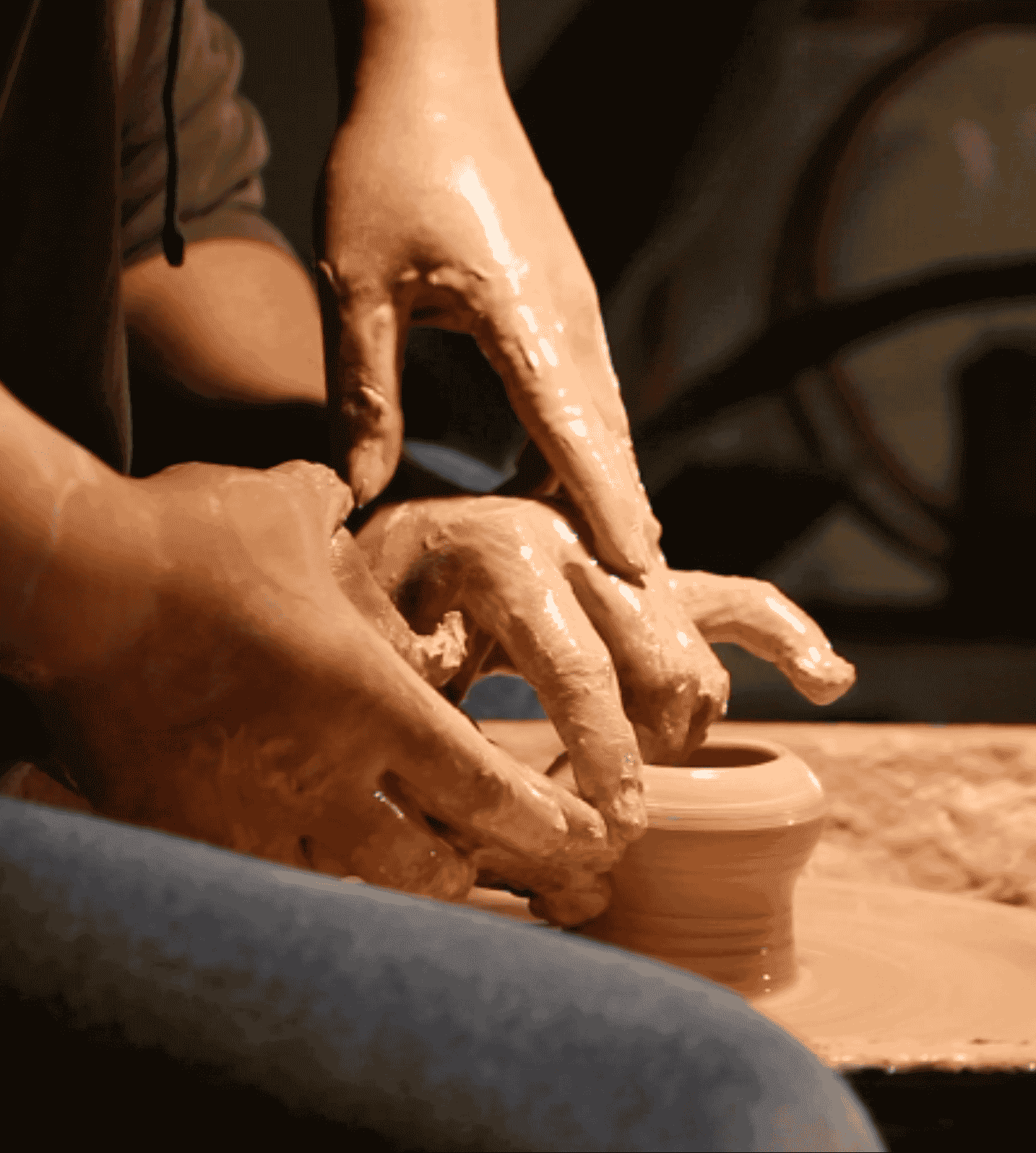 Hands shaping wet clay on a pottery wheel, creating a ceramic vase.
