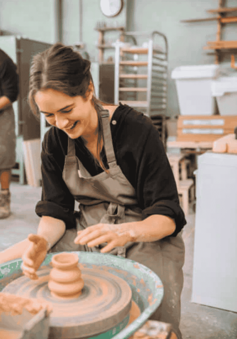 Woman shaping clay on pottery wheel in ceramics studio, smiling