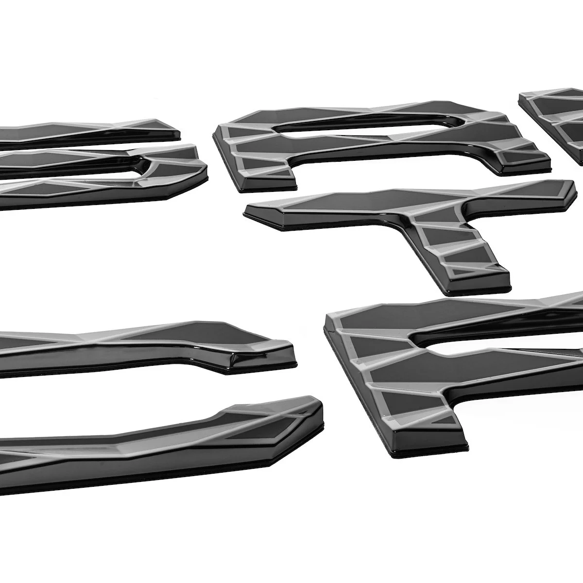 Close-up of glossy black and silver decorative car emblems spelling 'R' on a white background.