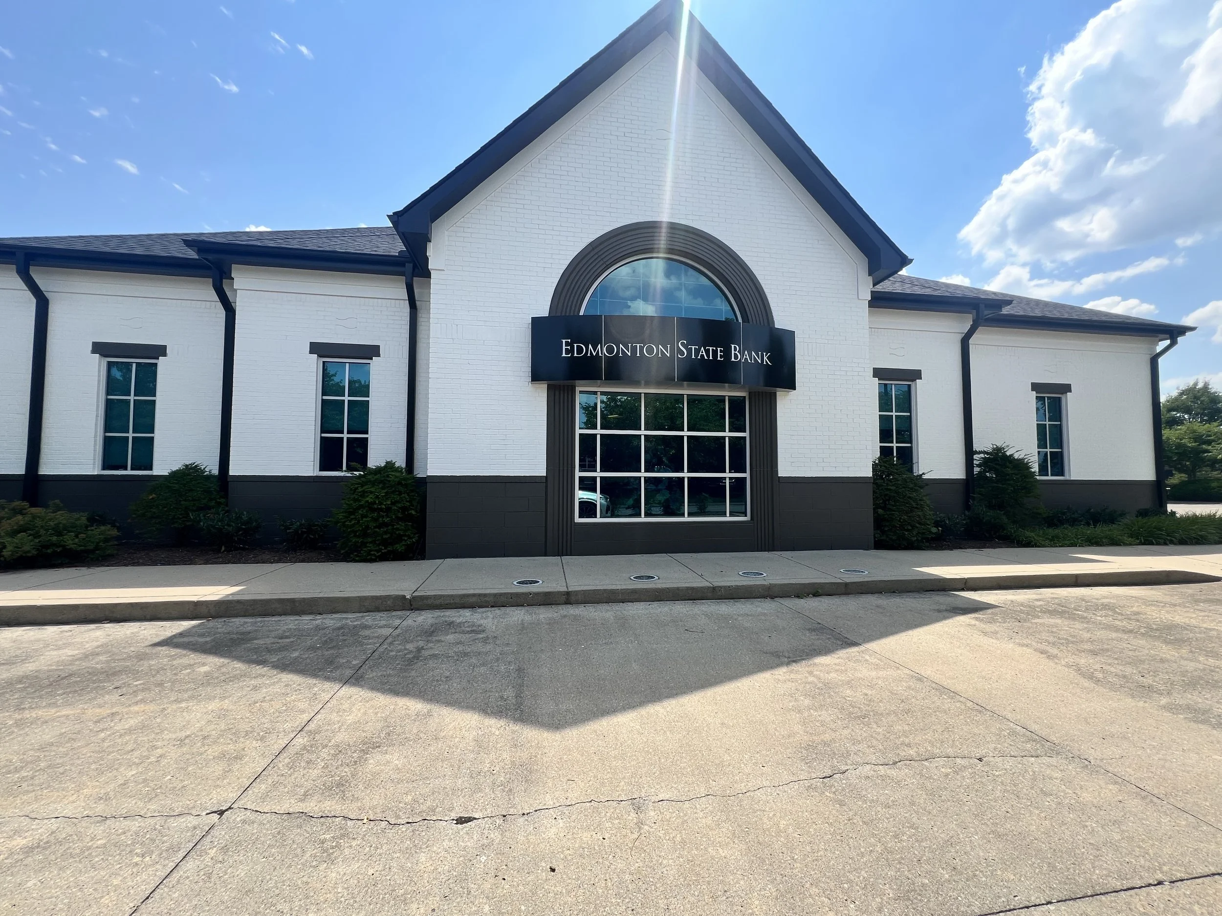 Exterior view of Edmonton State Bank building with white brick walls, dark trim, and a large arched window above the entrance, under a clear blue sky.