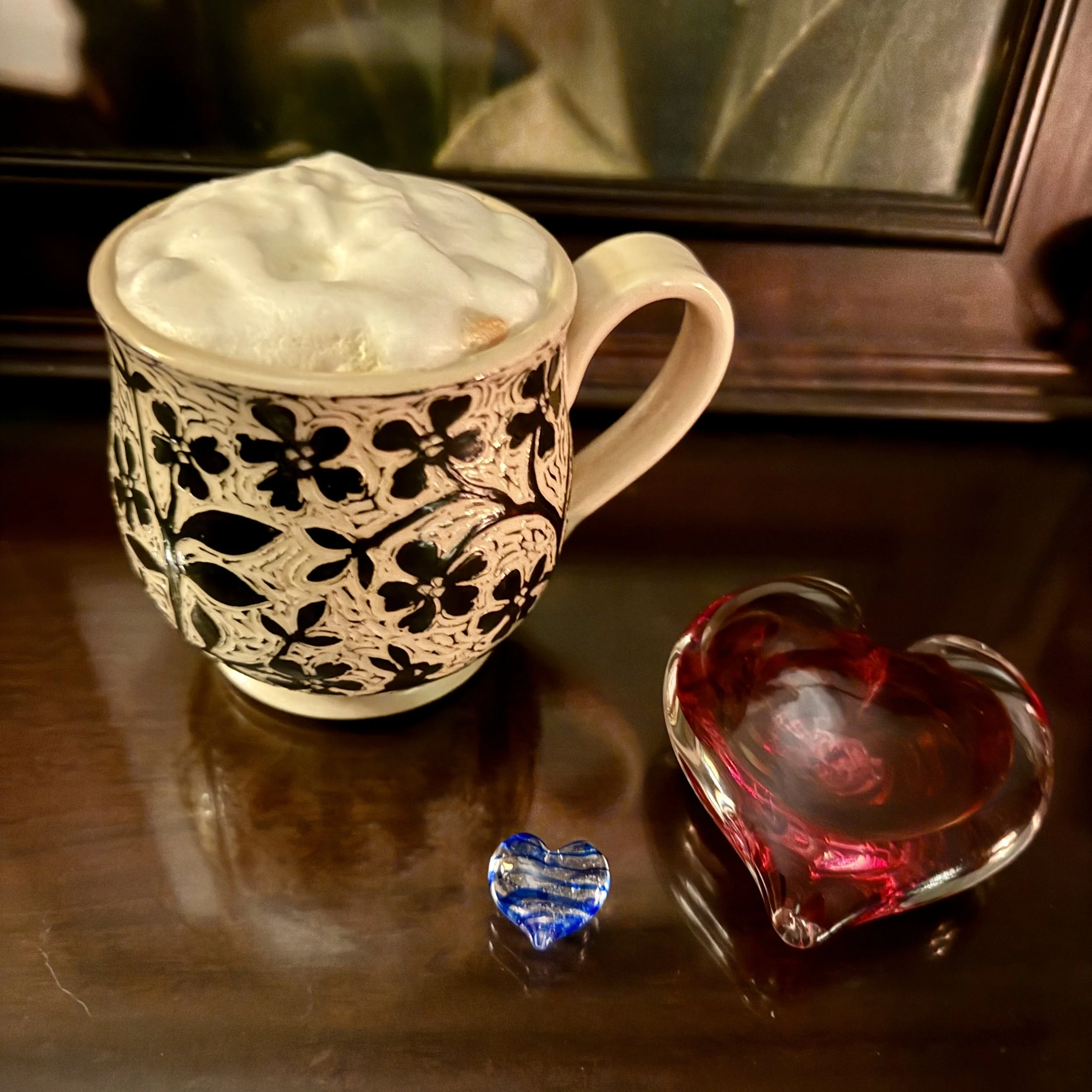 Coffee cup with creamy foam beside glass heart objects, warm morning light, peaceful reflective moment, personal lifestyle image for Studio Journal