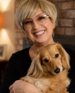 Warm portrait of a smiling woman holding a long-haired dachshund, cozy indoor setting, gentle and comforting tone, representing connection and heartfelt moments