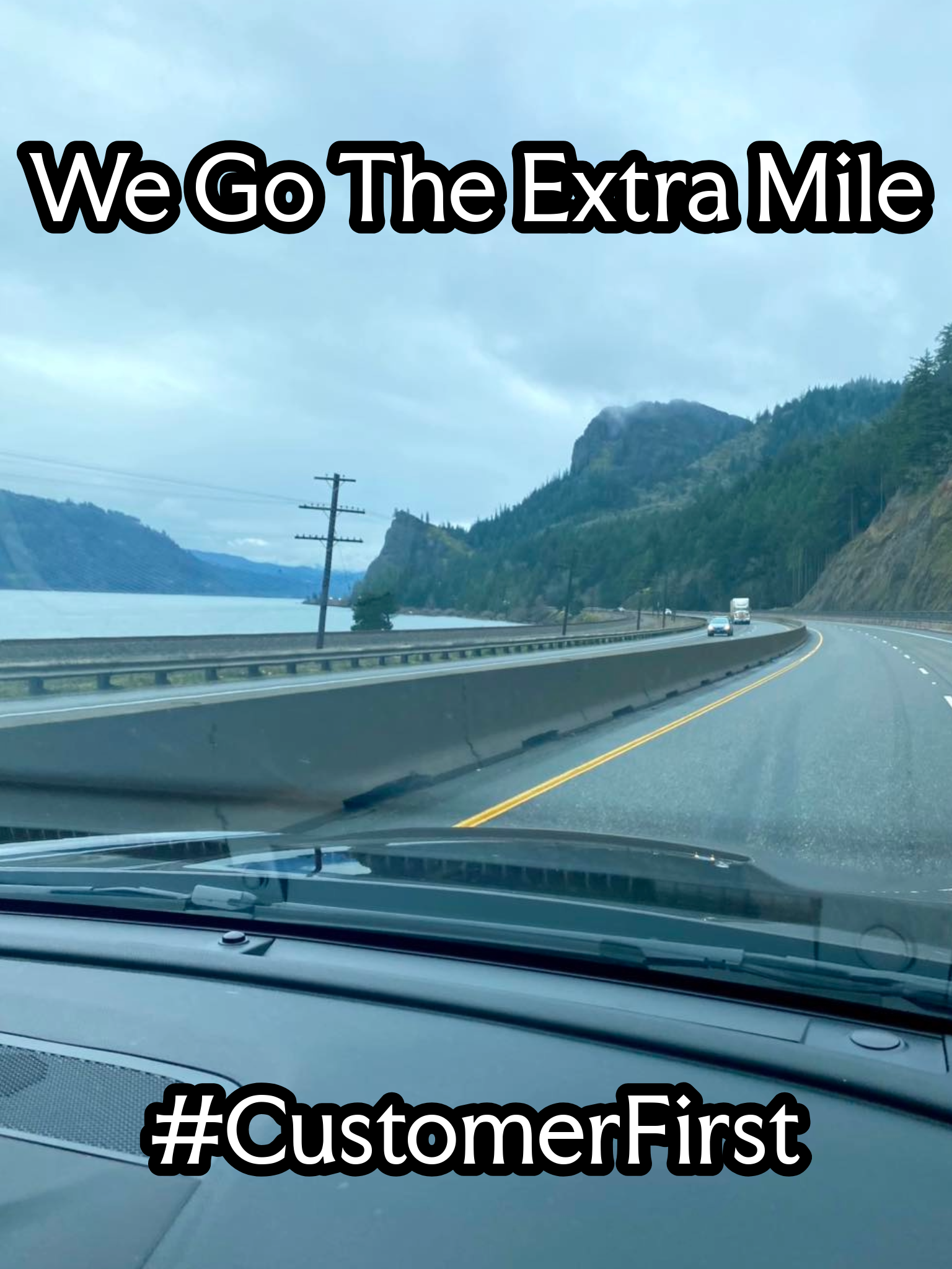 A scenic drive along a curving highway next to a body of water with mountains in the background, overlaid with bold black text that reads 'We Go The Extra Mile' and '#CustomerFirst'.