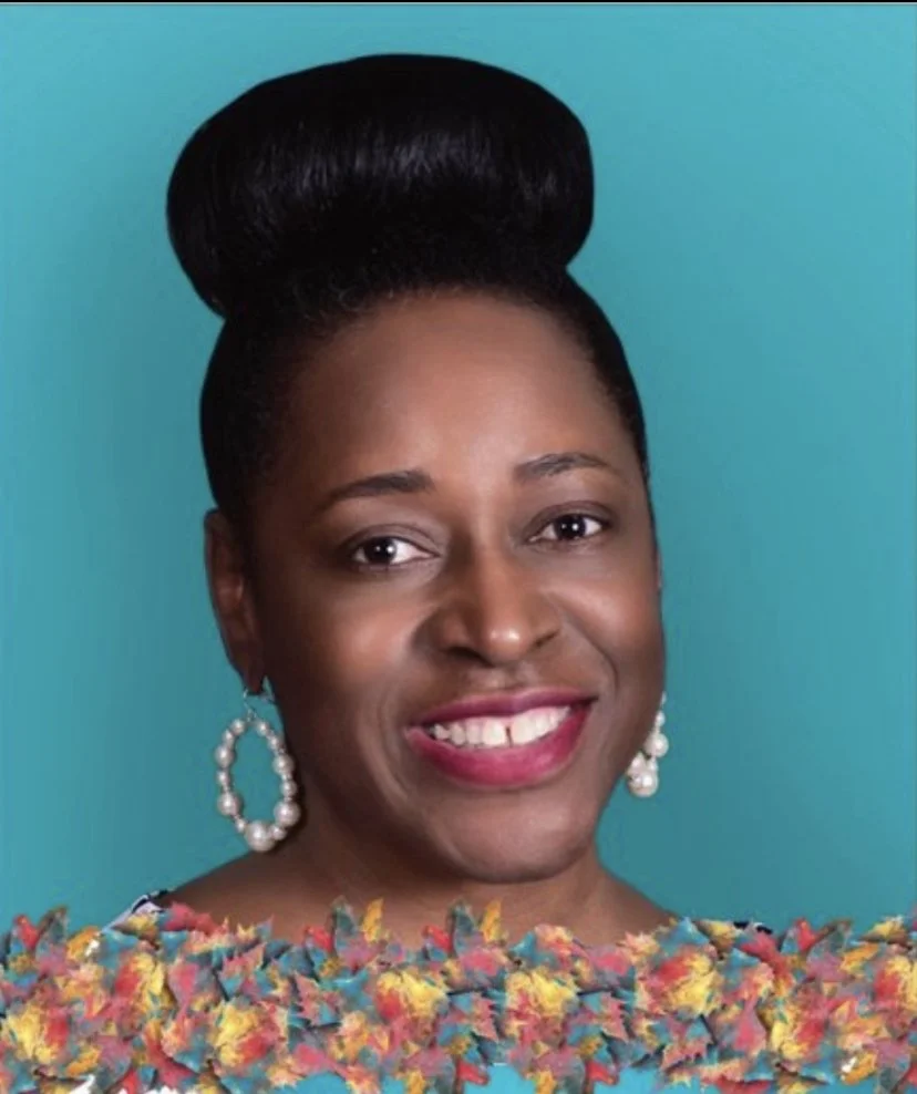 Portrait of a woman with a high bun hairstyle, wearing pearl earrings, a colorful textured top, and smiling against a blue background.