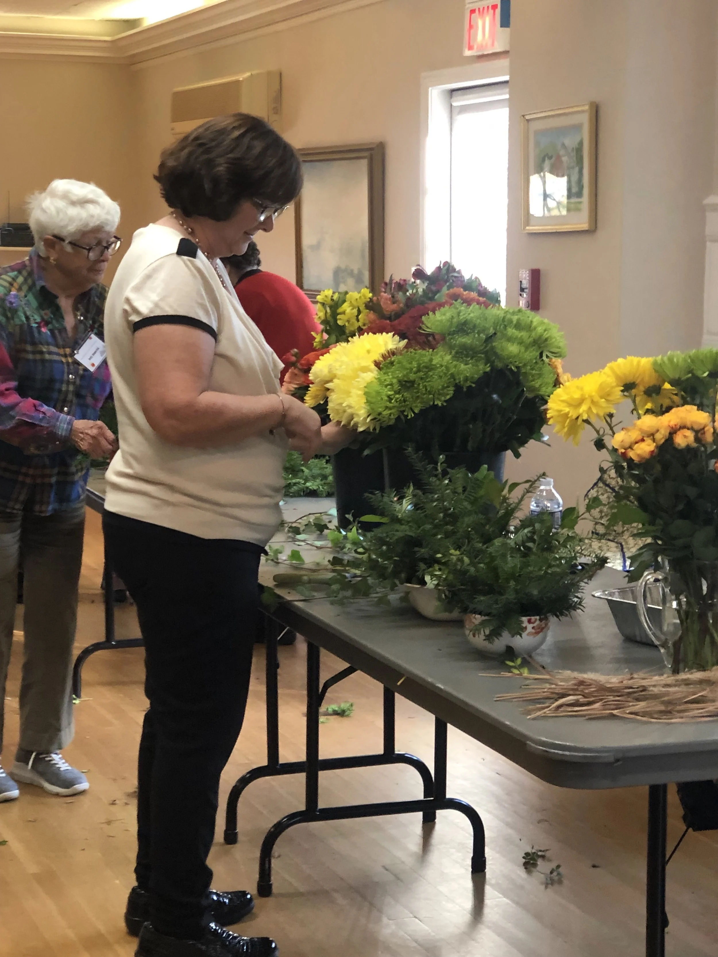 Women arranging a large bouquet of colorful flowers on a table indoors.