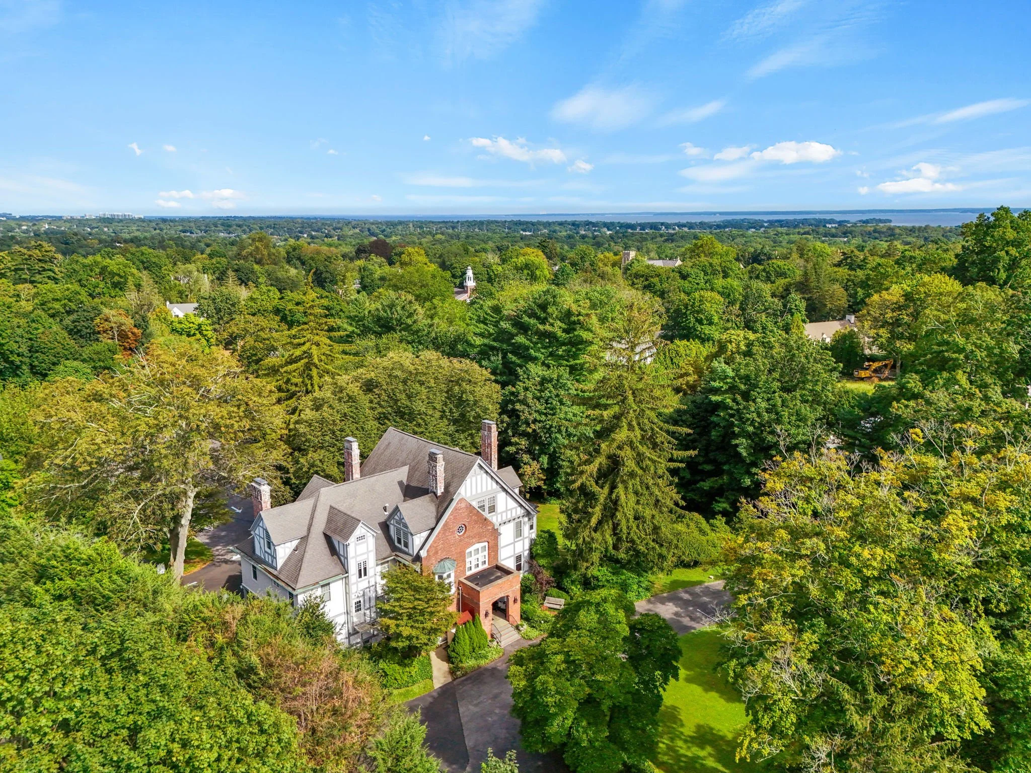 A large house surrounded by lush green trees in a suburban neighborhood, with a view of Lake Ontario and blue sky with clouds in the background.