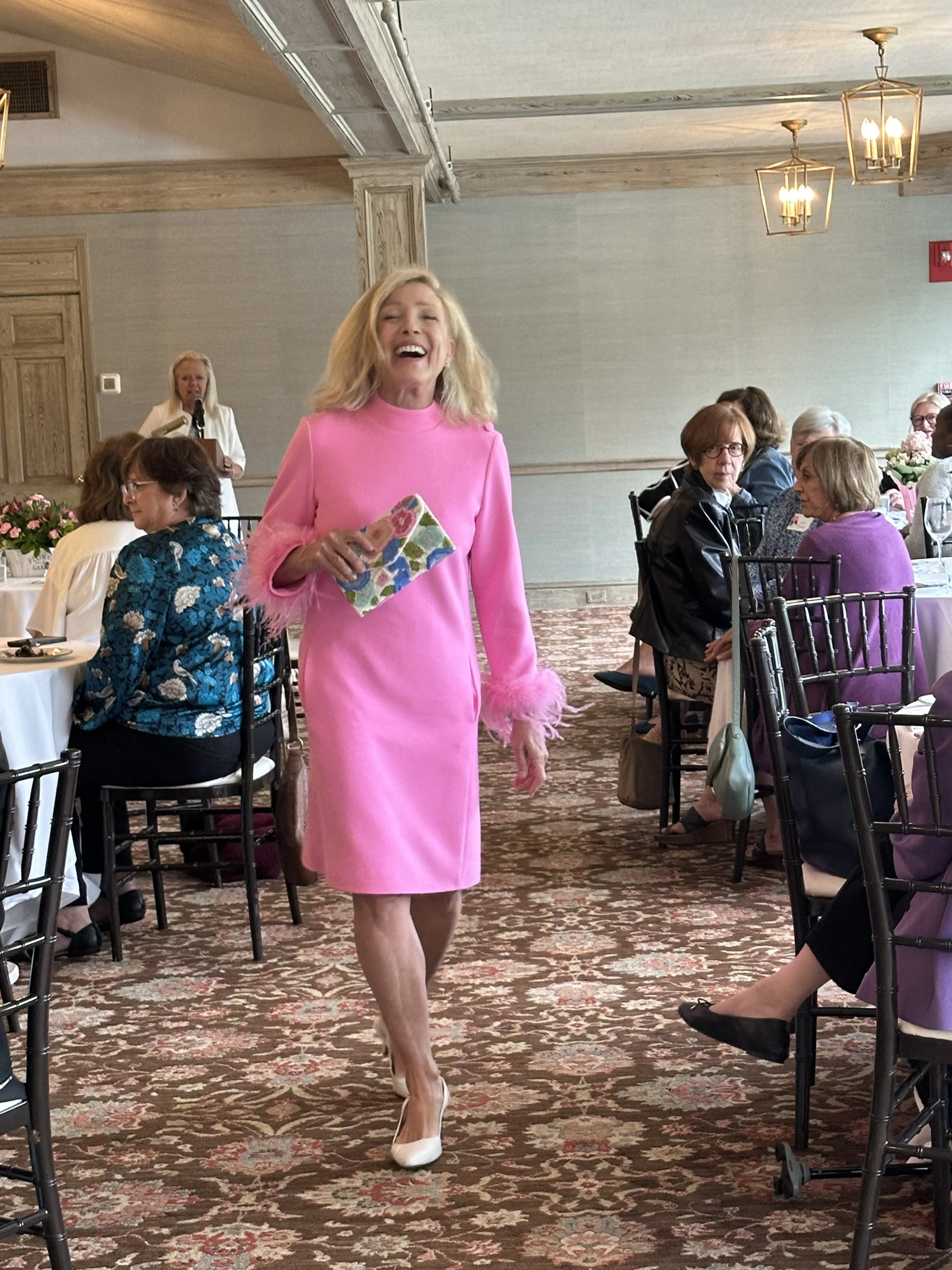 A woman in a bright pink dress walking through a banquet hall with seated guests at round tables.