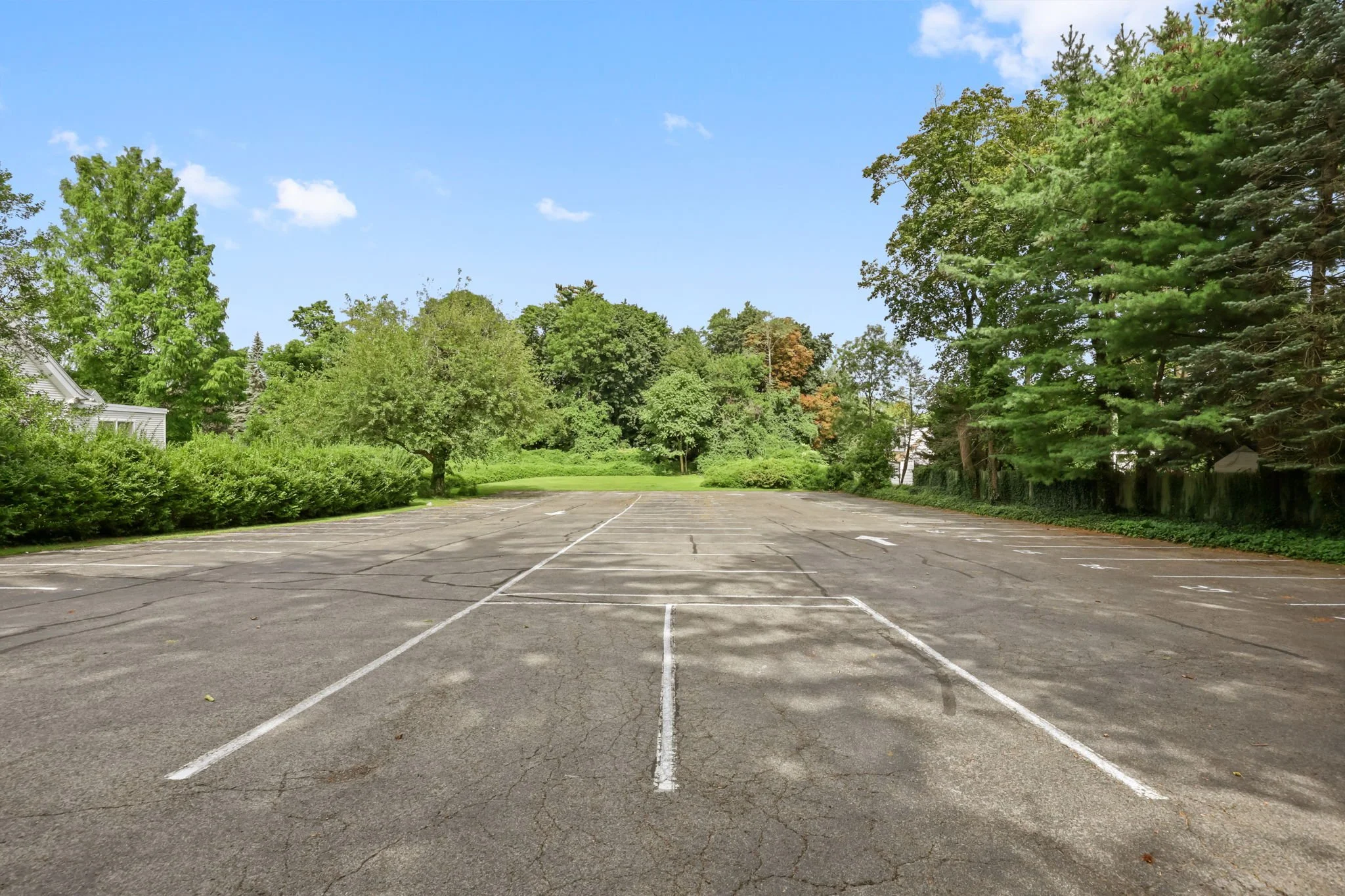 Empty parking lot surrounded by green trees, with a partly cloudy sky.