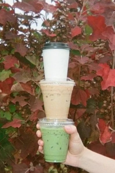a stack of coffee drinks and iced matcha latte in to go cups, outdoors