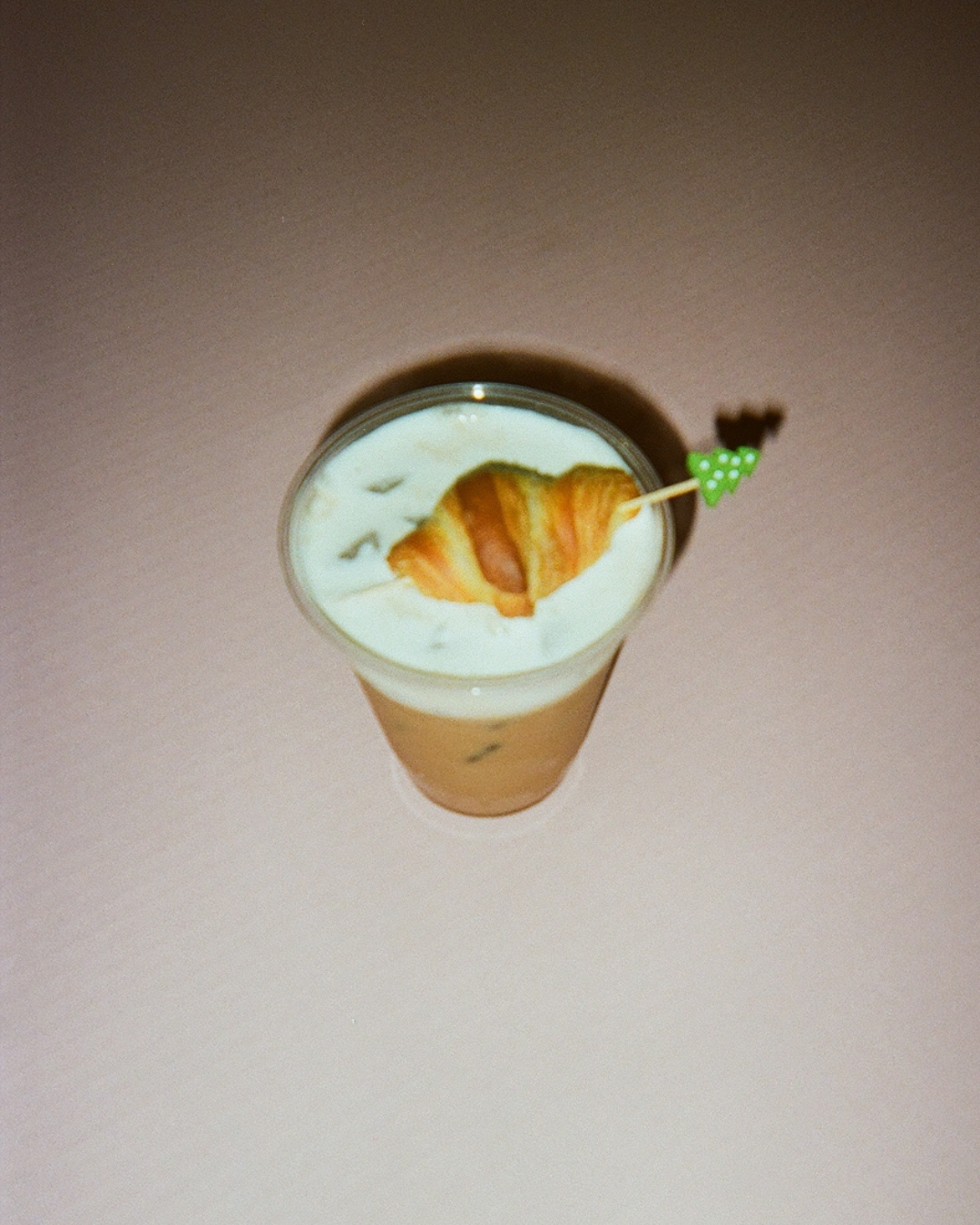 A tall glass of a creamy beverage with a croissant-shaped garnish and a small decorative pick with a green and white polka dot bow.