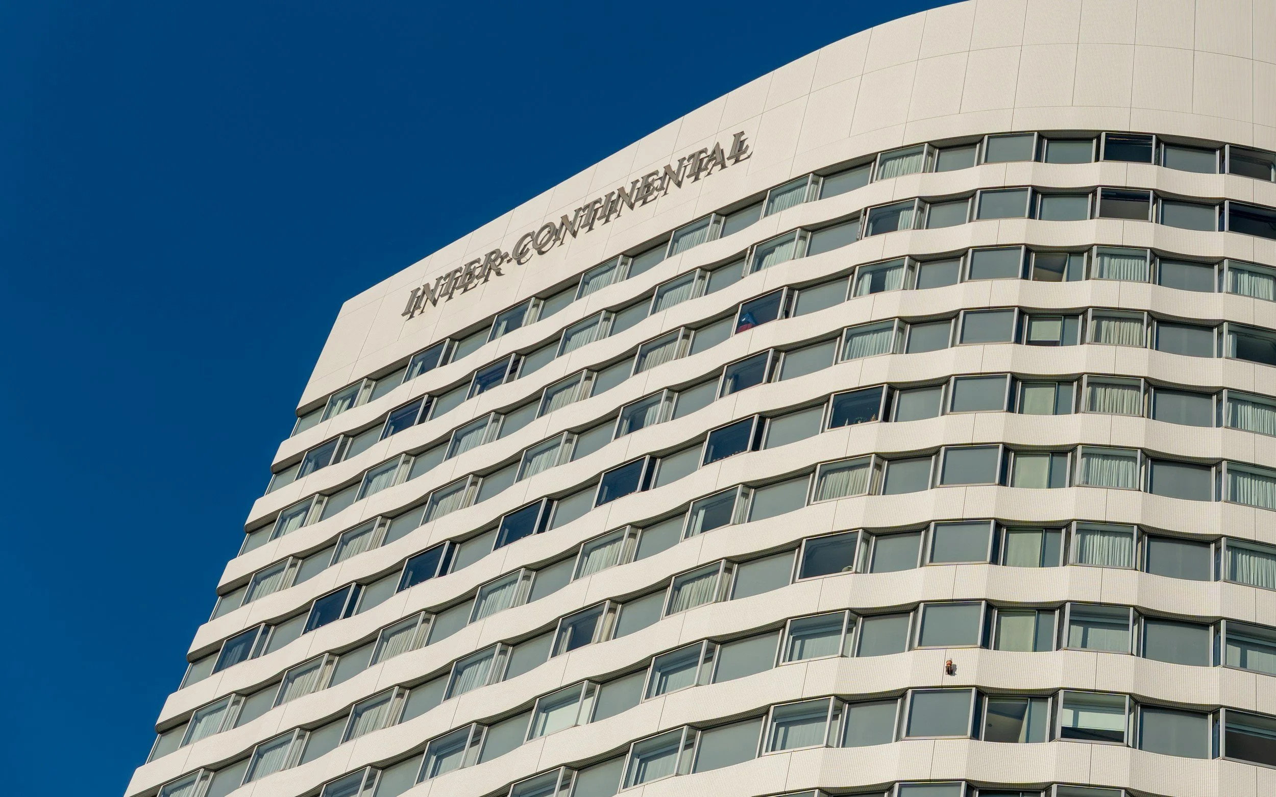 Exterior of a modern, high-rise building with rounded balconies and the words 'Innjersentimental' on the top facade, set against a clear blue sky.