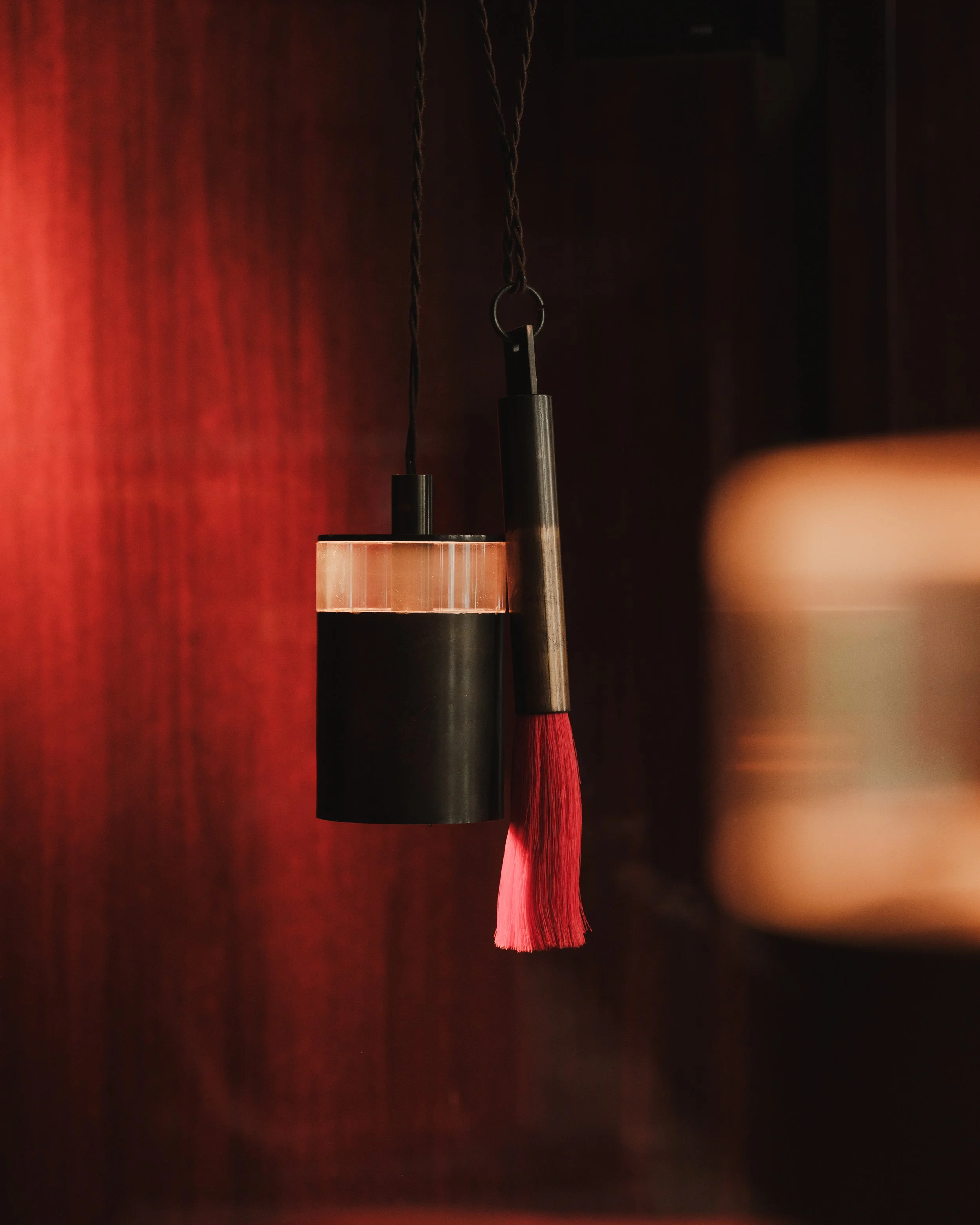 Close-up of hanging pendant light with a red tassel, against a dark background with reddish-brown walls.