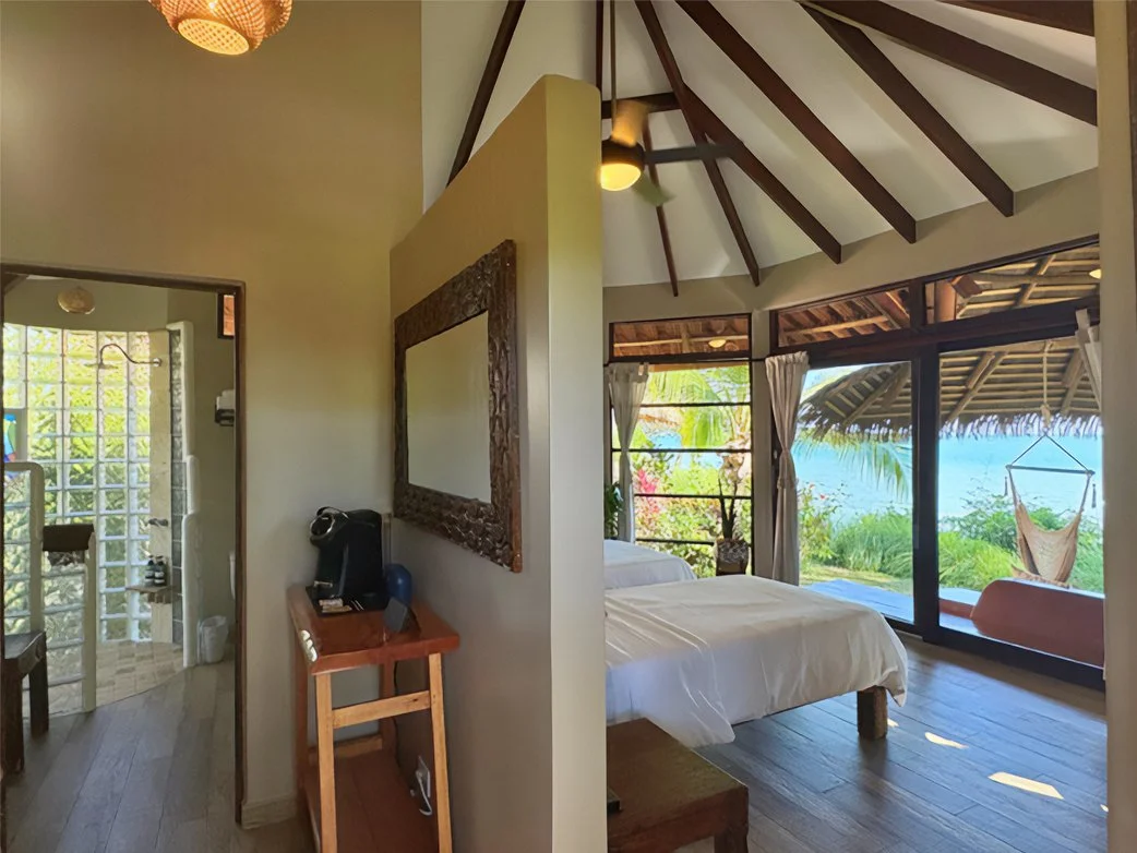 A Shared bedroom with large windows, two single beds, showing a view of the beach and ocean, a hammock swing outside.