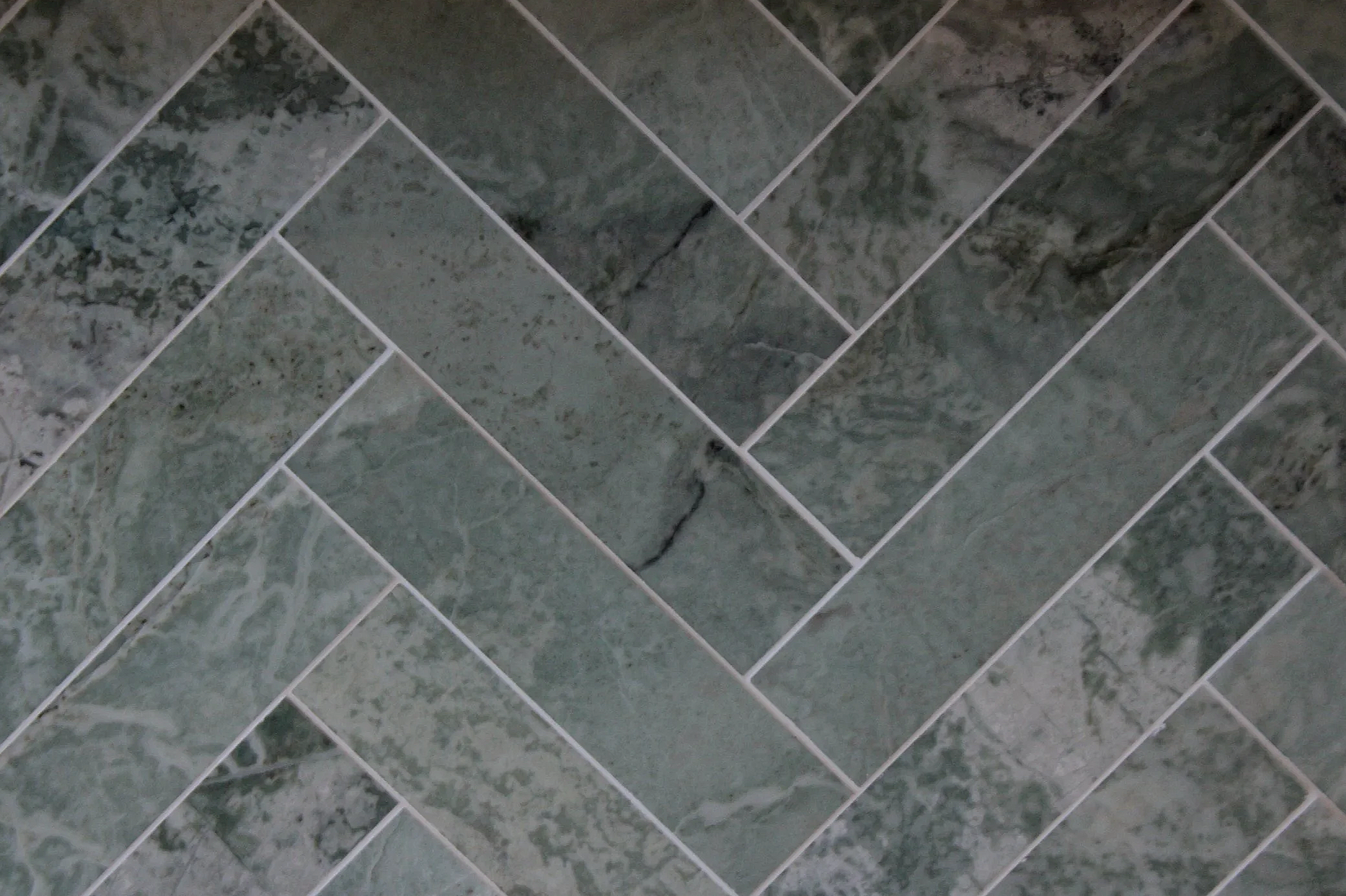 Close-up view of a wall with green marble tiles arranged in a herringbone pattern.
