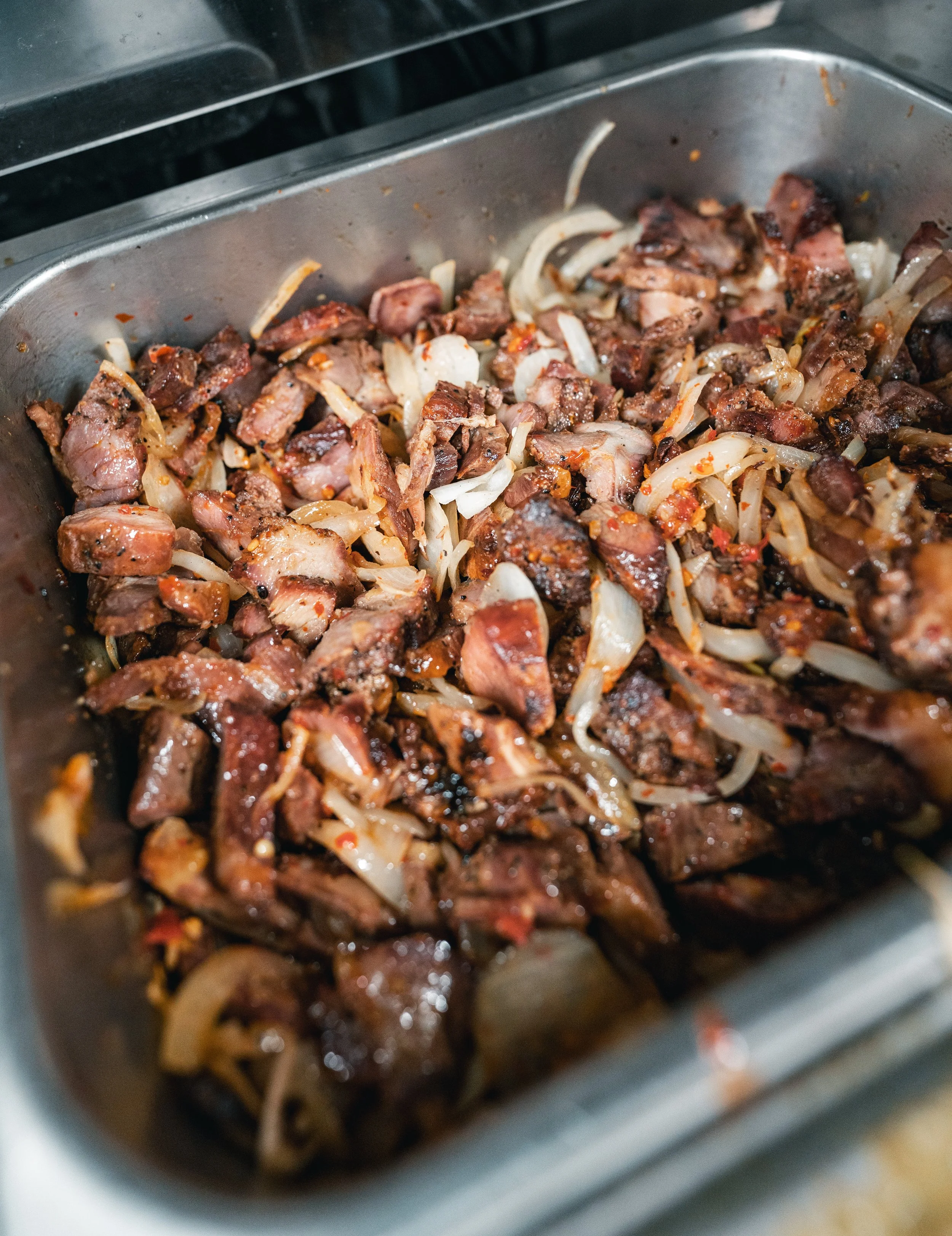 Close-up of cooked meat with onions in a metal container, possibly for a dish or meal.