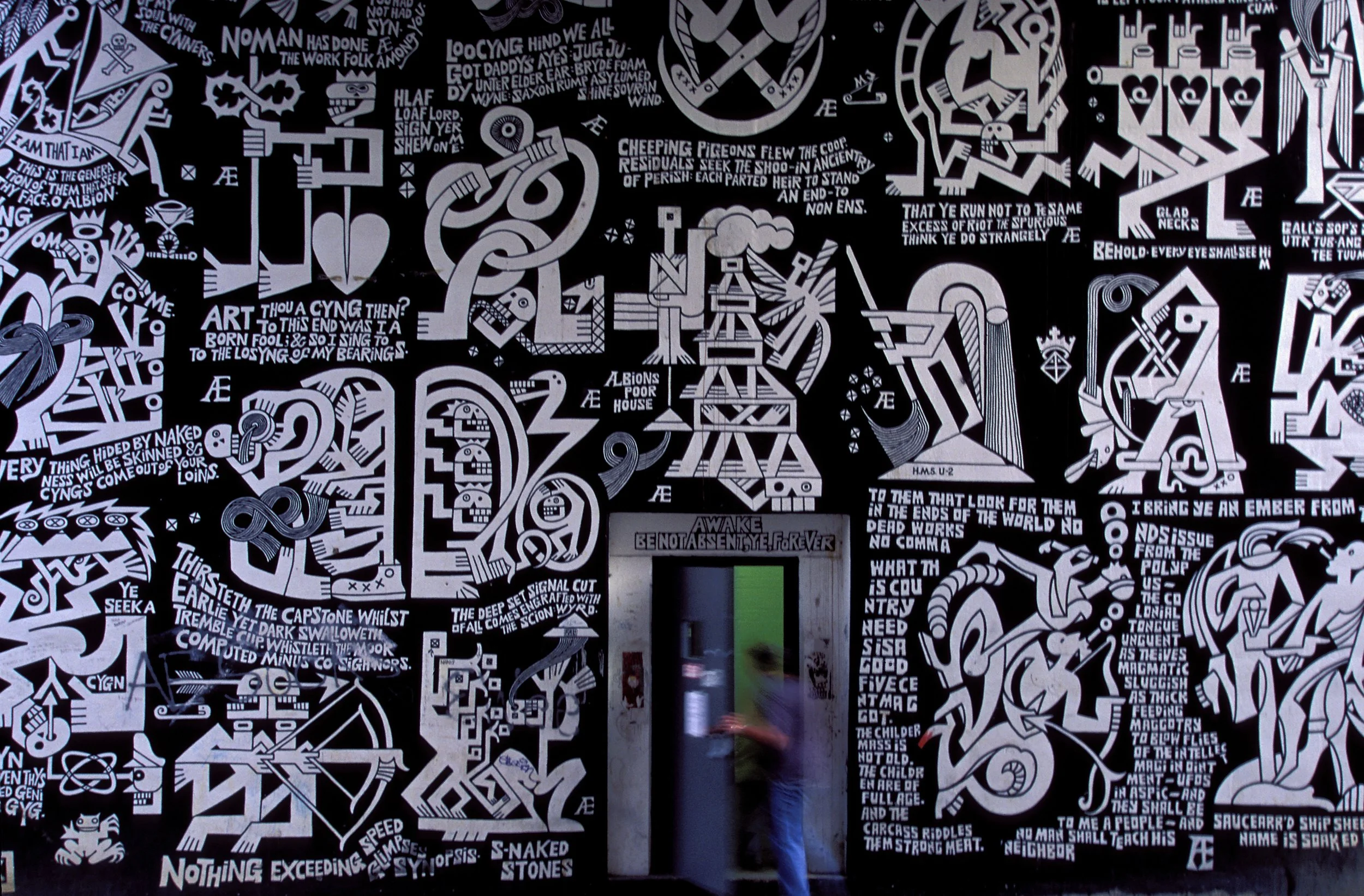 A student enters Seigfred Hall, home to Ohio University’s famed mural by the late art professor Æthelred Eldridge. Painted in 1965–66, the large black-and-white work—featuring bold, blocky forms and cryptic phrases inspired by poet William Blake—has