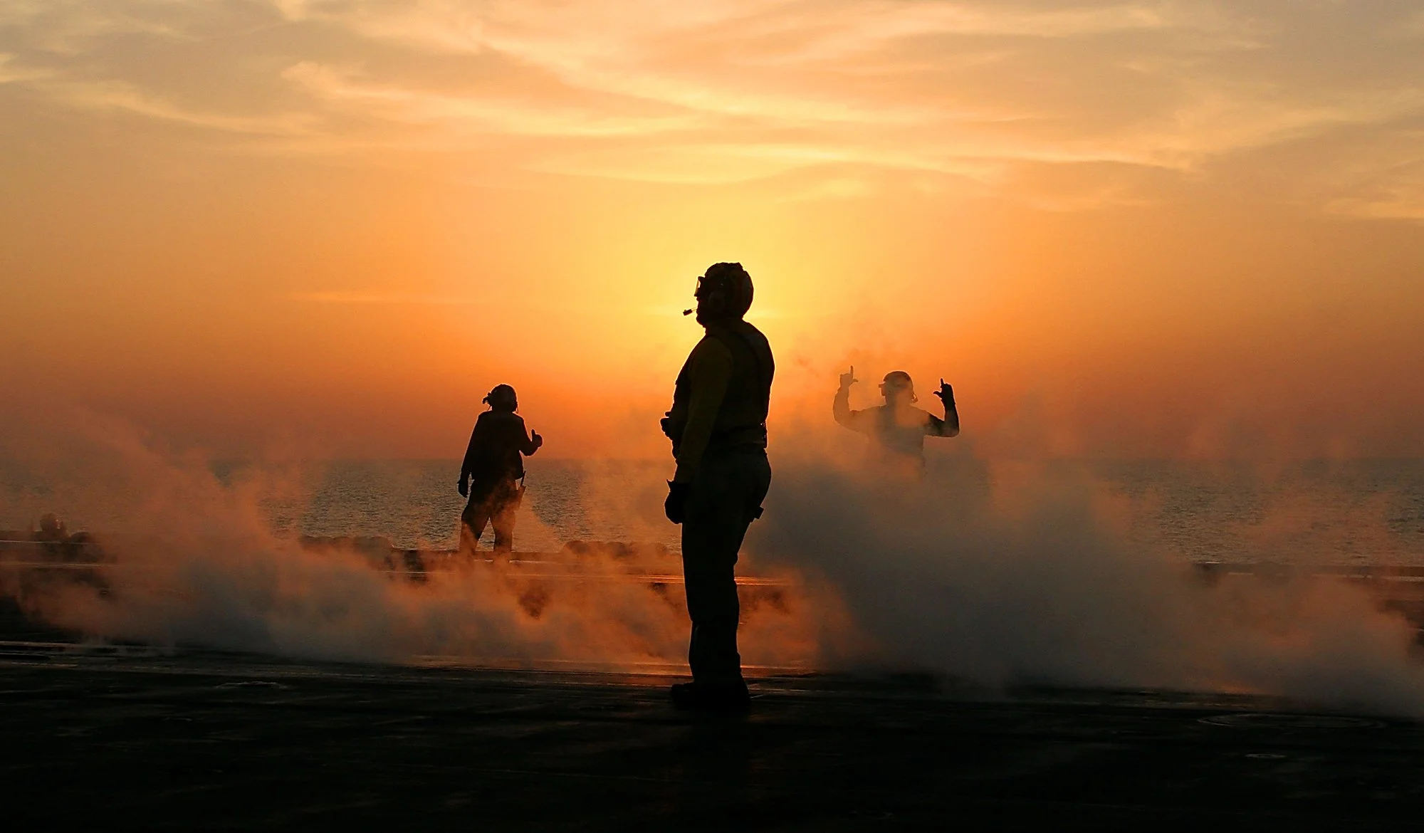 Lt. Cmdr. ABHC Wilson Theodore, center, and two crew members signal clearance on the flight deck of the USS Theodore Roosevelt following a jet’s launch for an evening bombing mission in the Persian Gulf. The Theodore Roosevelt remains an active Nimit