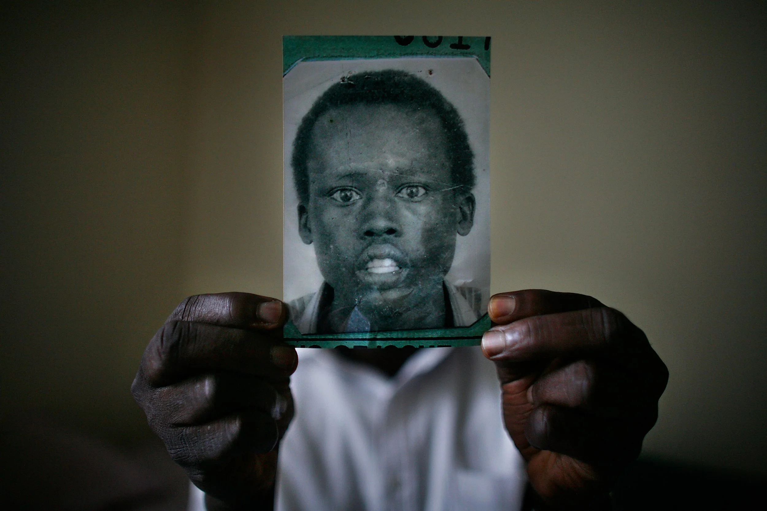 Dut Akech, one of the Lost Boys of Sudan, holds the official refugee identification photo taken in Kenya after fleeing his homeland.