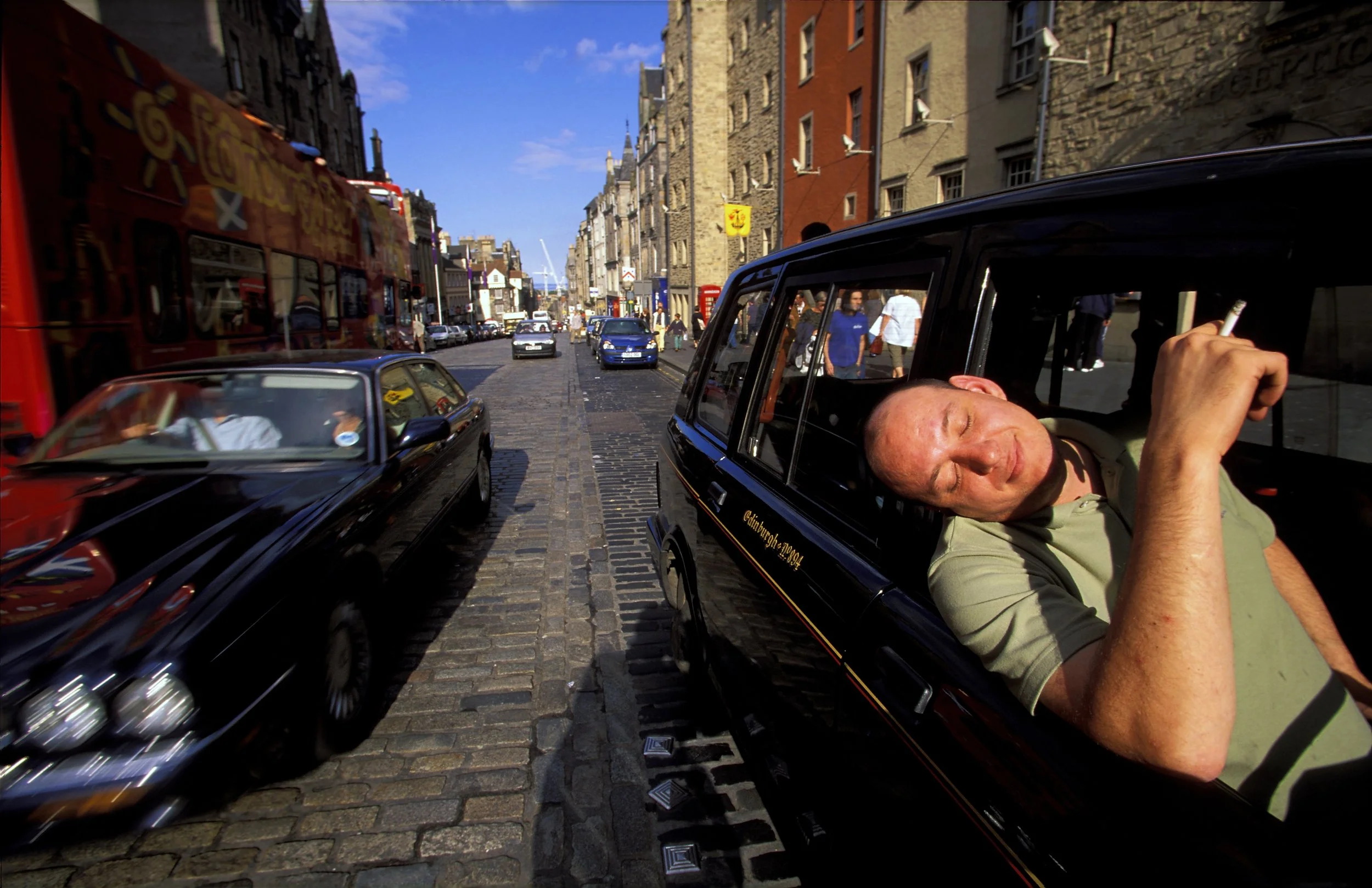 On Edinburgh’s historic Royal Mile, a taxi driver enjoys a cigarette in rare sunshine during what became a record-breaking rainfall season. The Royal Mile, stretching from Edinburgh Castle to the Palace of Holyroodhouse, is the city’s most famous str