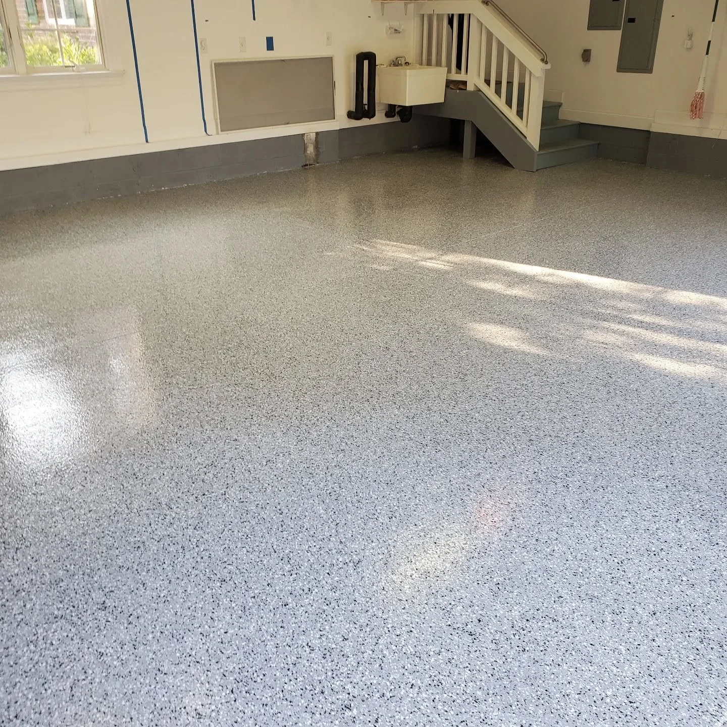 Empty garage with speckled gray epoxy floor, white walls, a staircase, and a small sink.
